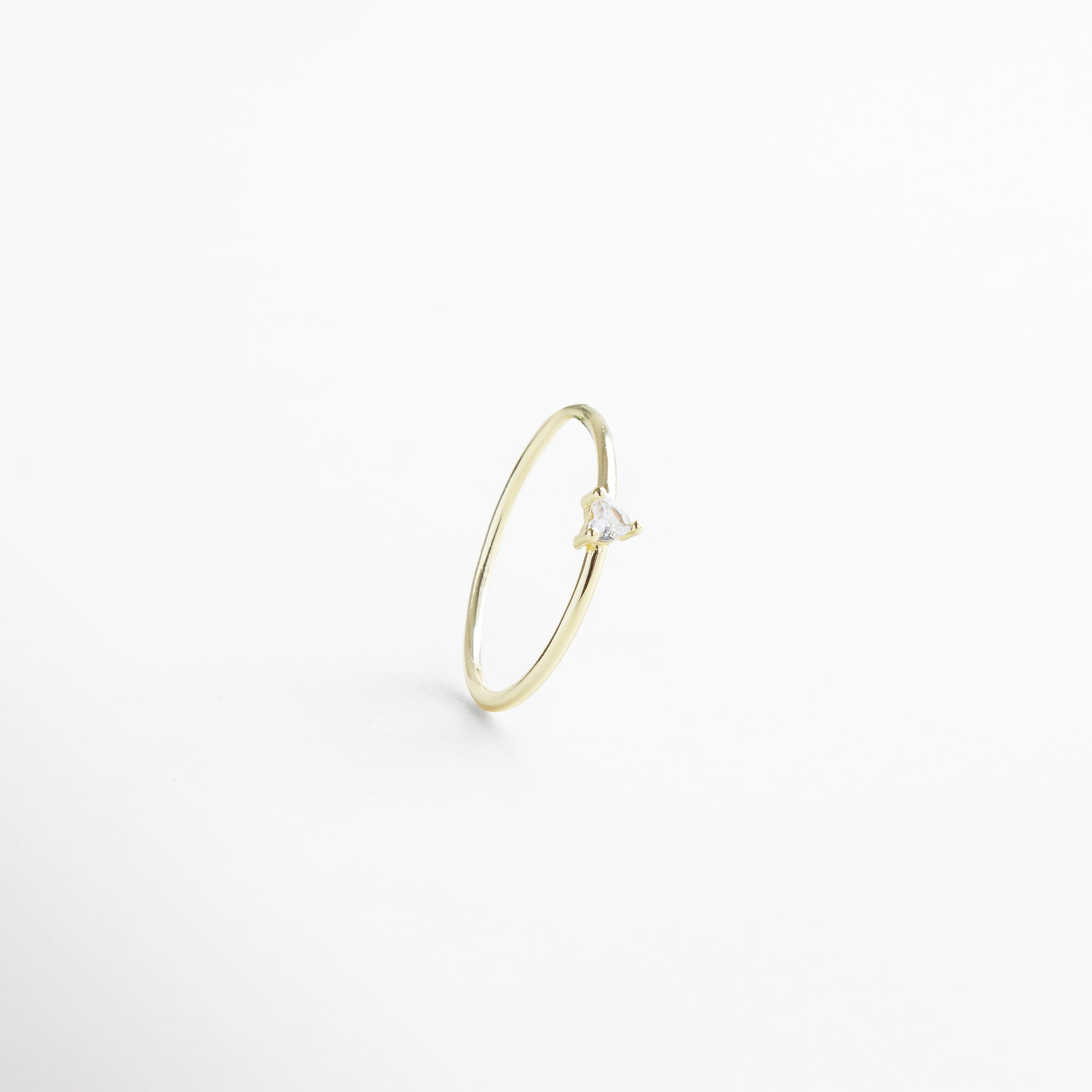 Anillo dorado delgado visto de frente, con pequeña piedra en forma de corazón en el centro. Vista frontal del anillo Heart dorado, diseño delicado y romántico sobre fondo neutro. Anillo fino en tono dorado con piedra central en forma de corazón, fotografía frontal completa. Primer plano frontal del anillo Heart dorado, destacando su piedra central y acabado elegante. Anillo dorado con piedra en forma de corazón, visto de frente con diseño sutil y femenino.