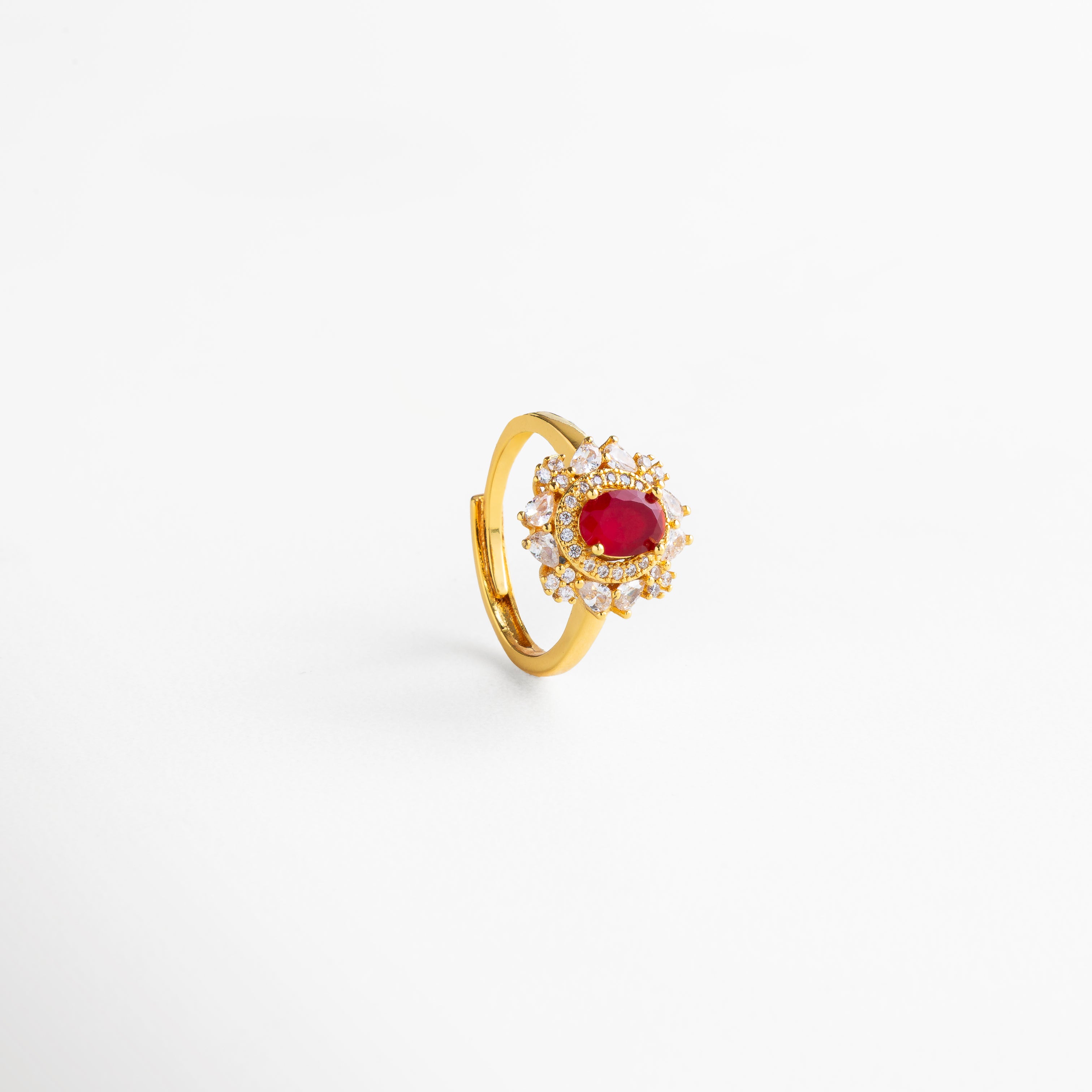 Vista lateral del anillo en cobre con baño de oro 18K, piedra roja central en forma ovalada rodeada de zirconias cúbicas transparentes, diseño ajustable de estilo atemporal con acabado pulido que aporta elegancia y fuerza a cualquier look.