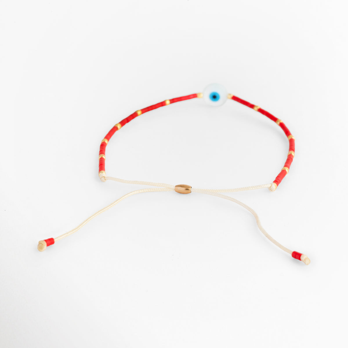 Vista posterior de la Pulsera Roja Ojo Turco mostrando el cierre de nudo corredizo en hilo natural beige con remates en hilo rojo, Acercamiento al mecanismo de tejido ajustable y la extensión de los cordones sobre fondo blanco, Detalle de la terminación posterior de la pulsera amuleto que permite adaptar el diámetro a cualquier muñeca, Muestra del sistema deslizante de hilo natural con aplique dorado central de ajuste.