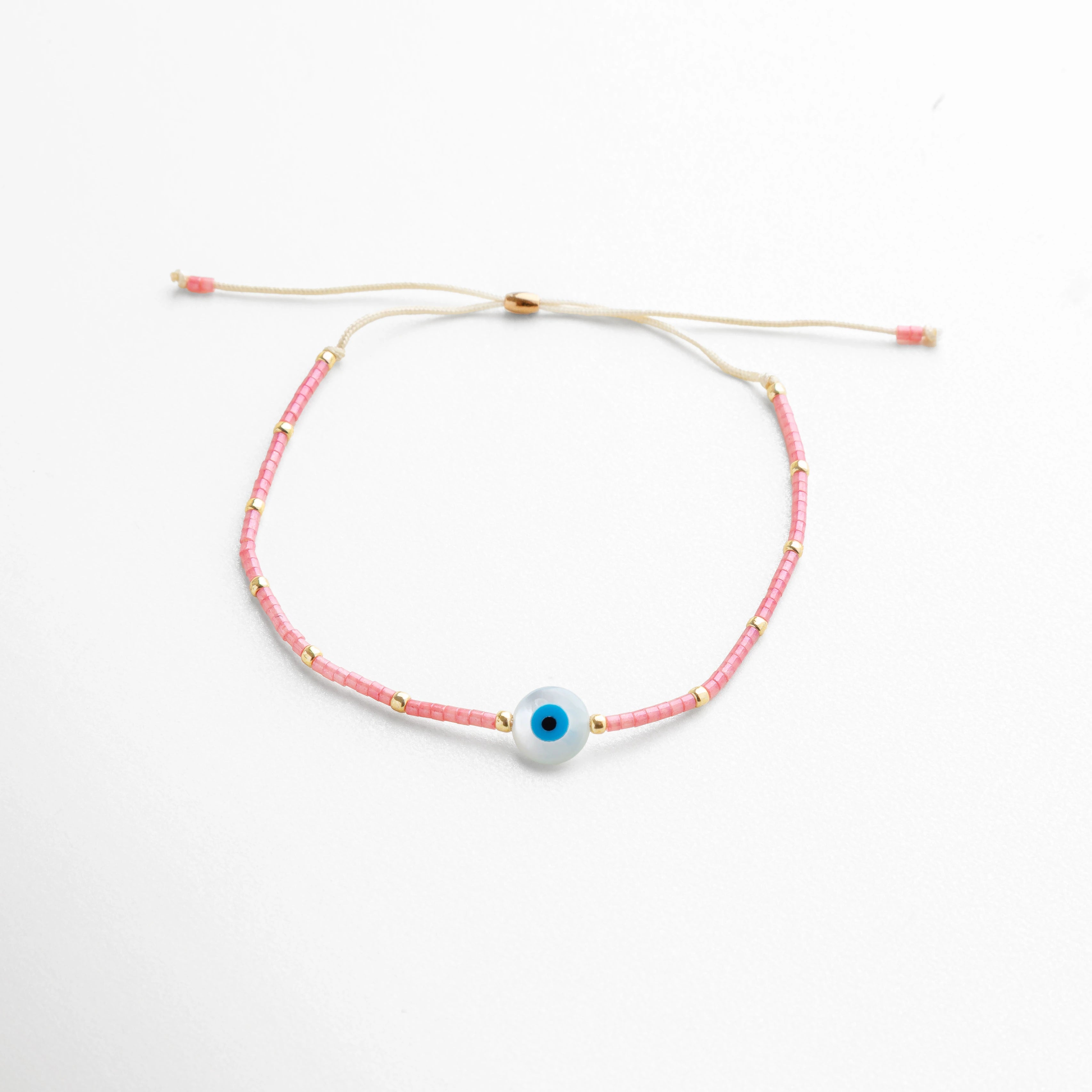 Pulsera rosa con cuentas de vidrio y dije central de ojo turco azul, protección y estilo, Pulsera ajustable de hilo beige con cuentas rosas y ojo turco, amuleto contra malas energías, Pulsera artesanal rosa con ojo turco, joyería moderna de protección y moda.
