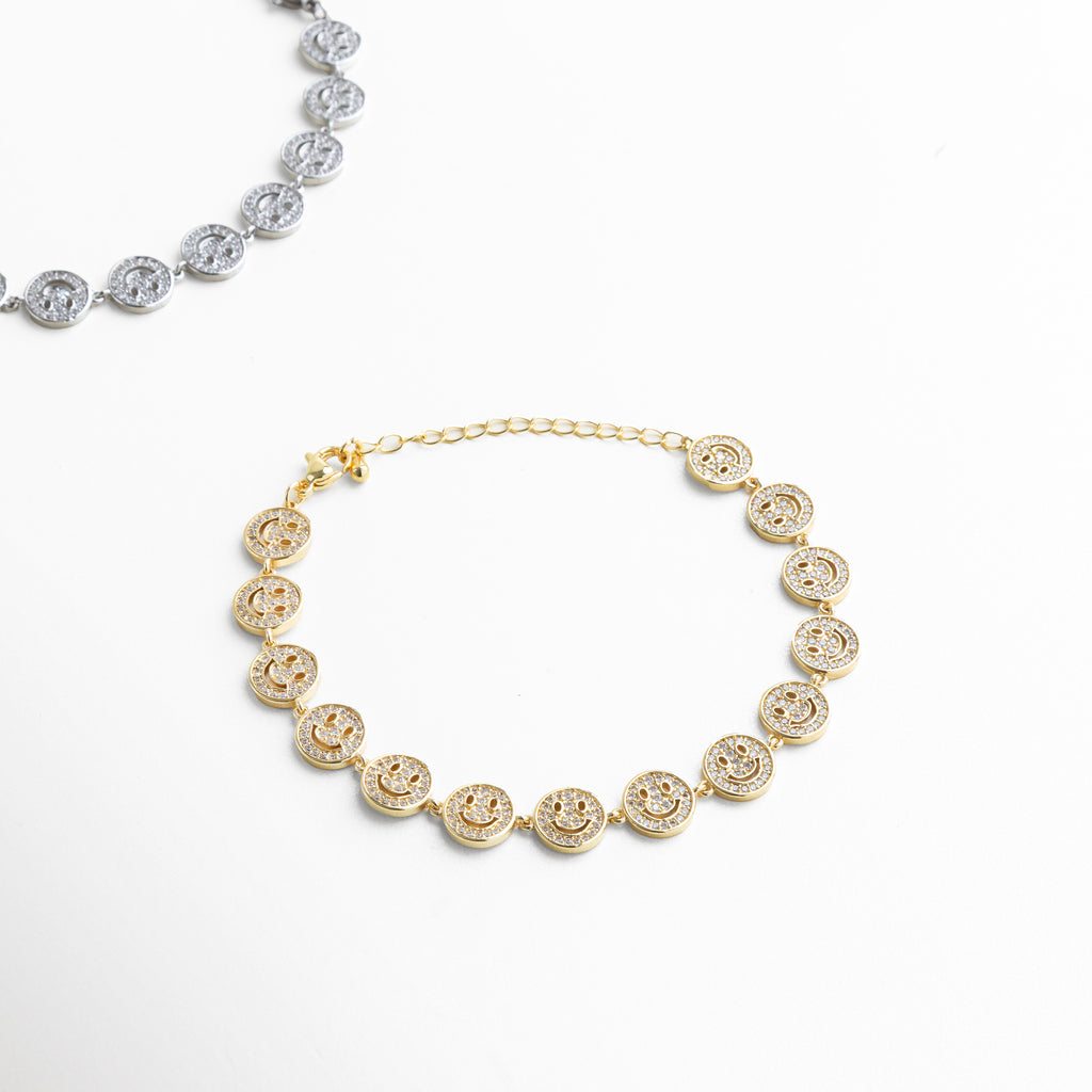 Primer plano del dije de carita sonriente con zirconias, Detalle de incrustaciones brillantes en el dije dorado, Textura y acabado enchapado en oro 18K, Contorno circular del dije con piedras facetadas, Diseño pulido y simétrico del dije sonriente