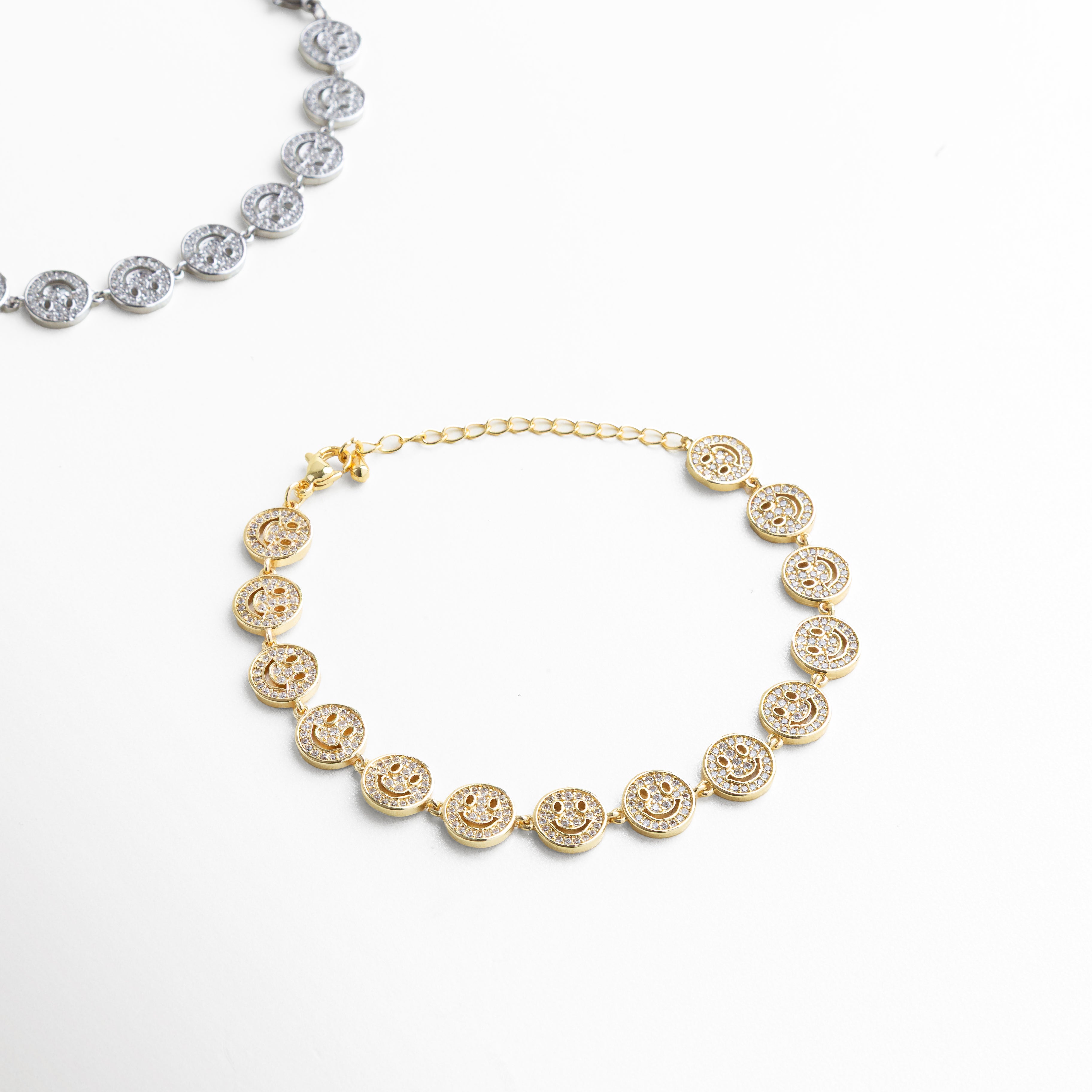 Primer plano del dije de carita sonriente con zirconias, Detalle de incrustaciones brillantes en el dije dorado, Textura y acabado enchapado en oro 18K, Contorno circular del dije con piedras facetadas, Diseño pulido y simétrico del dije sonriente