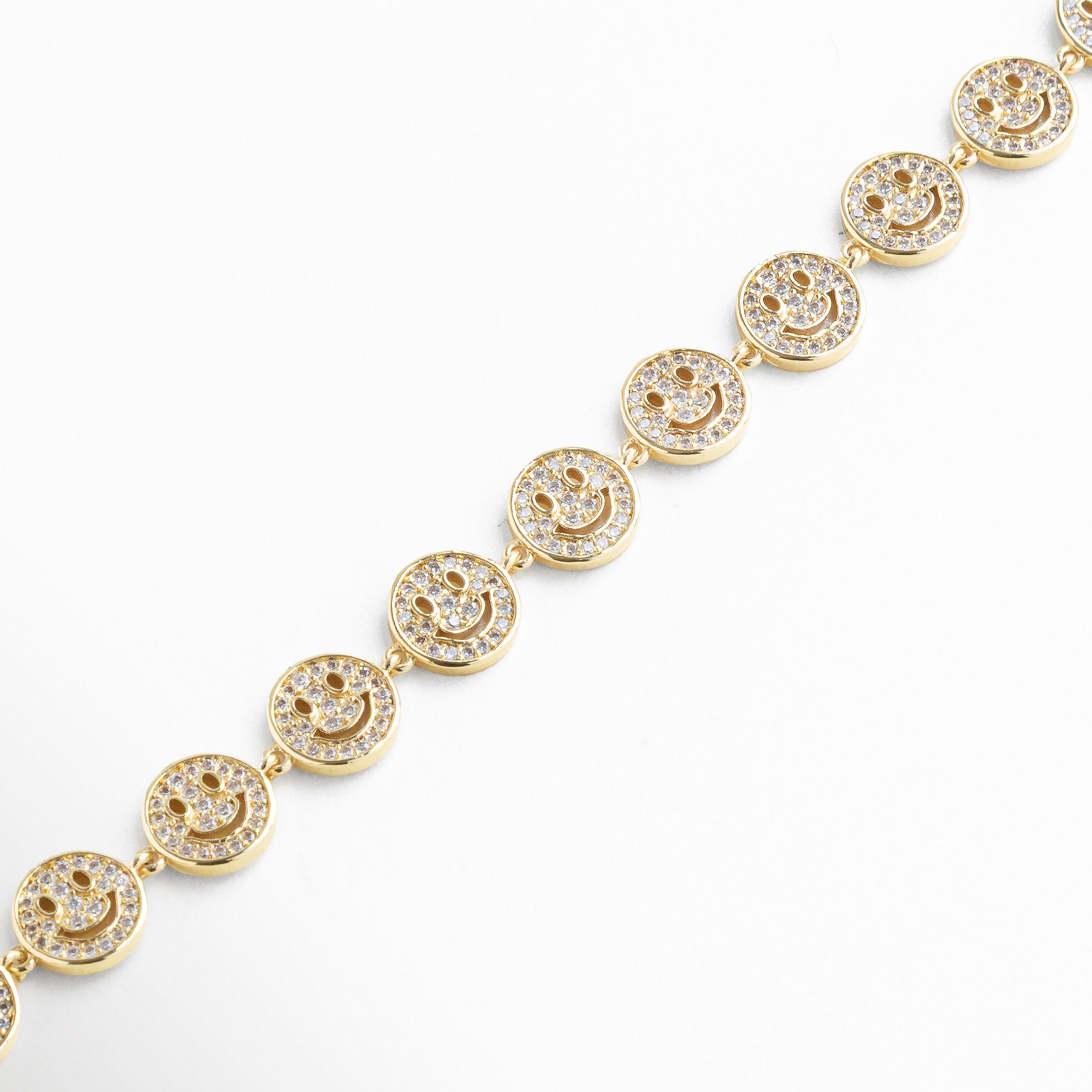 Acercamiento a la sonrisa con brillo de zirconias, Luz reflejada en piedras y metal dorado, Detalle del engaste de cada zirconia, Relieve de ojos y boca en el dije, Unión entre dije y cadena dorada