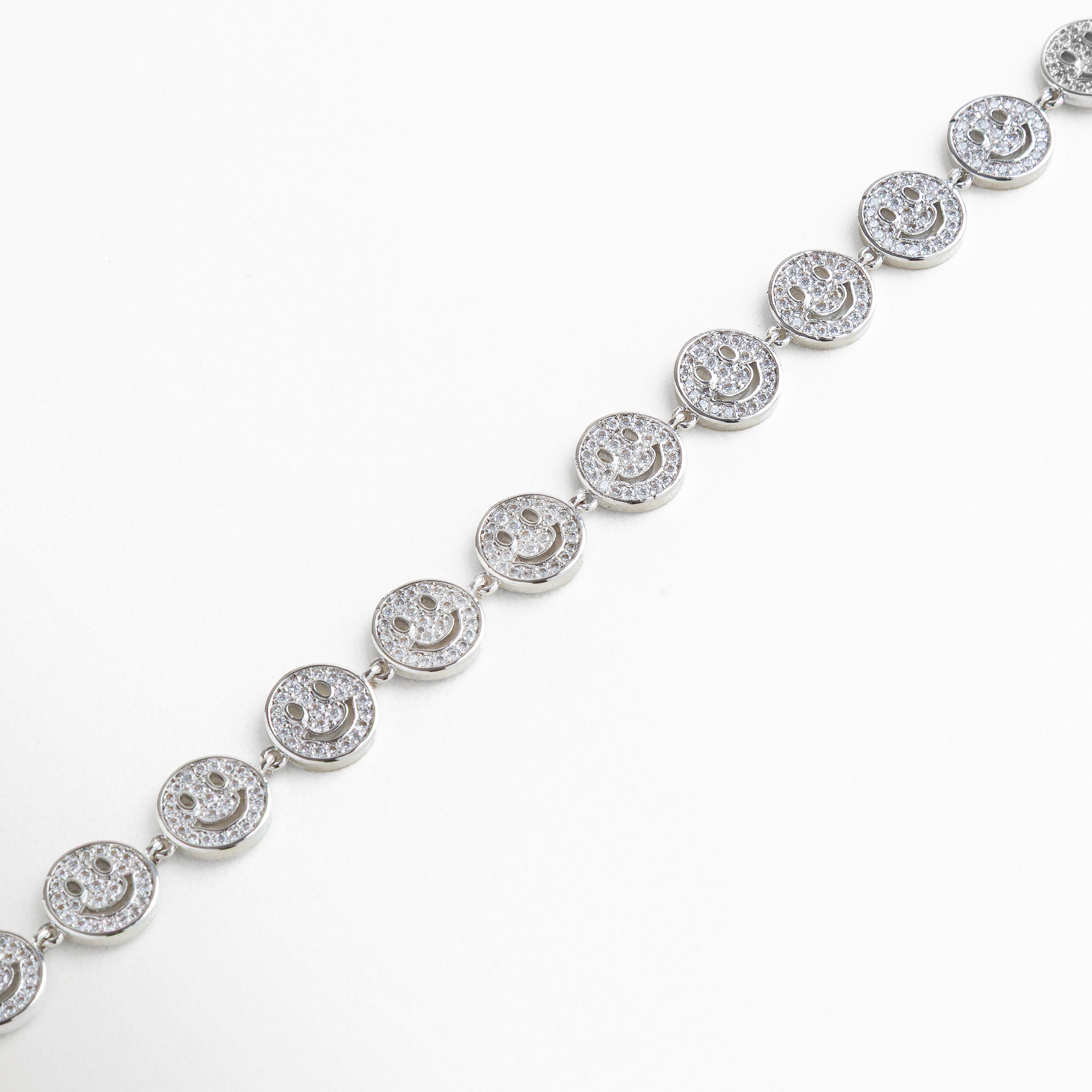 Acercamiento a la sonrisa con brillo de zirconias, Luz reflejada en piedras y metal plateado, Detalle del engaste de cada zirconia, Relieve de ojos y boca en el dije, Unión entre dije y cadena plateada