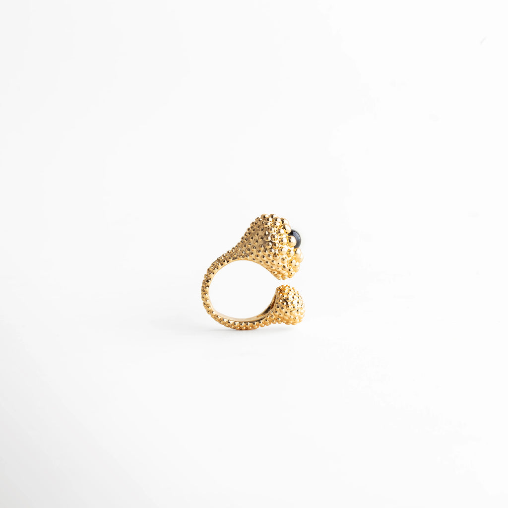 Anillo dorado texturizado con doble esfera y piedra negra, diseño abierto con acabado pulido, joyería moderna y original.