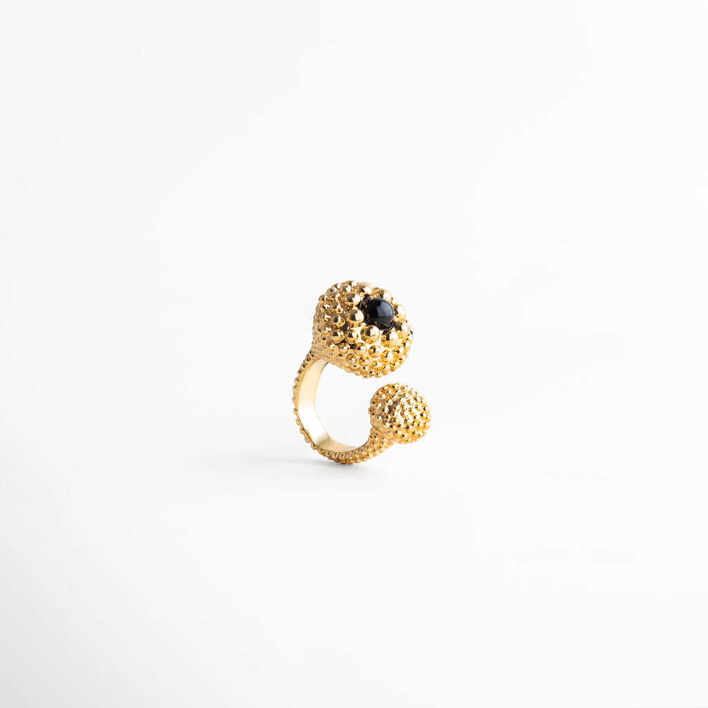 Anillo dorado abierto con textura esférica y piedra negra central, diseño moderno y elegante con acabado brillante, joya contemporánea ideal para looks sofisticados.