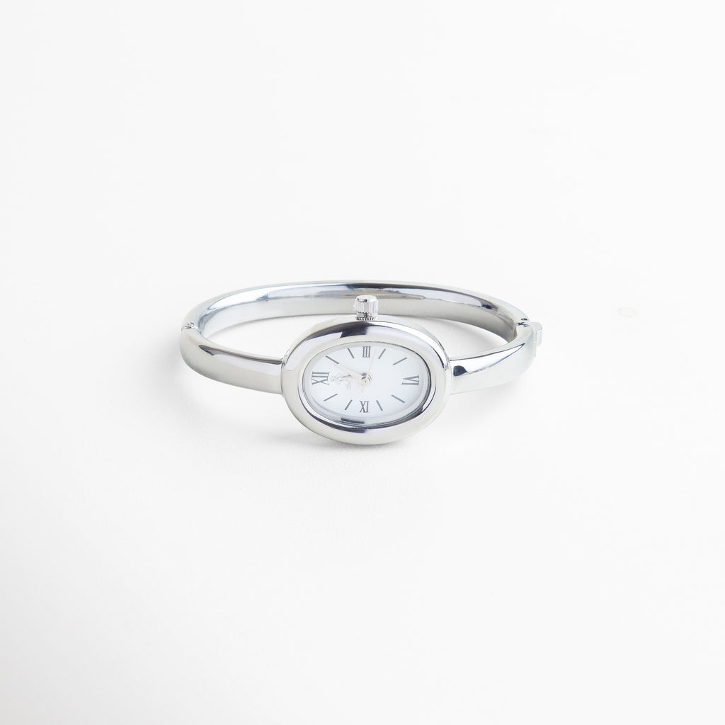 Vista superior del Reloj Braccialetto plateado, mostrando su diámetro de 6 cm y diseño limpio en forma de pulsera. Toma cenital del reloj tipo brazalete en acero plateado, con vitrina de 2 cm y cuerpo estilizado. Reloj Braccialetto visto desde arriba, con diseño metálico brillante y estructura delgada de 0.3 cm. Perspectiva superior del reloj rígido plateado, con líneas curvas y diseño minimalista. Vista desde arriba del Reloj Braccialetto en acero inoxidable, destacando su forma de brazalet
