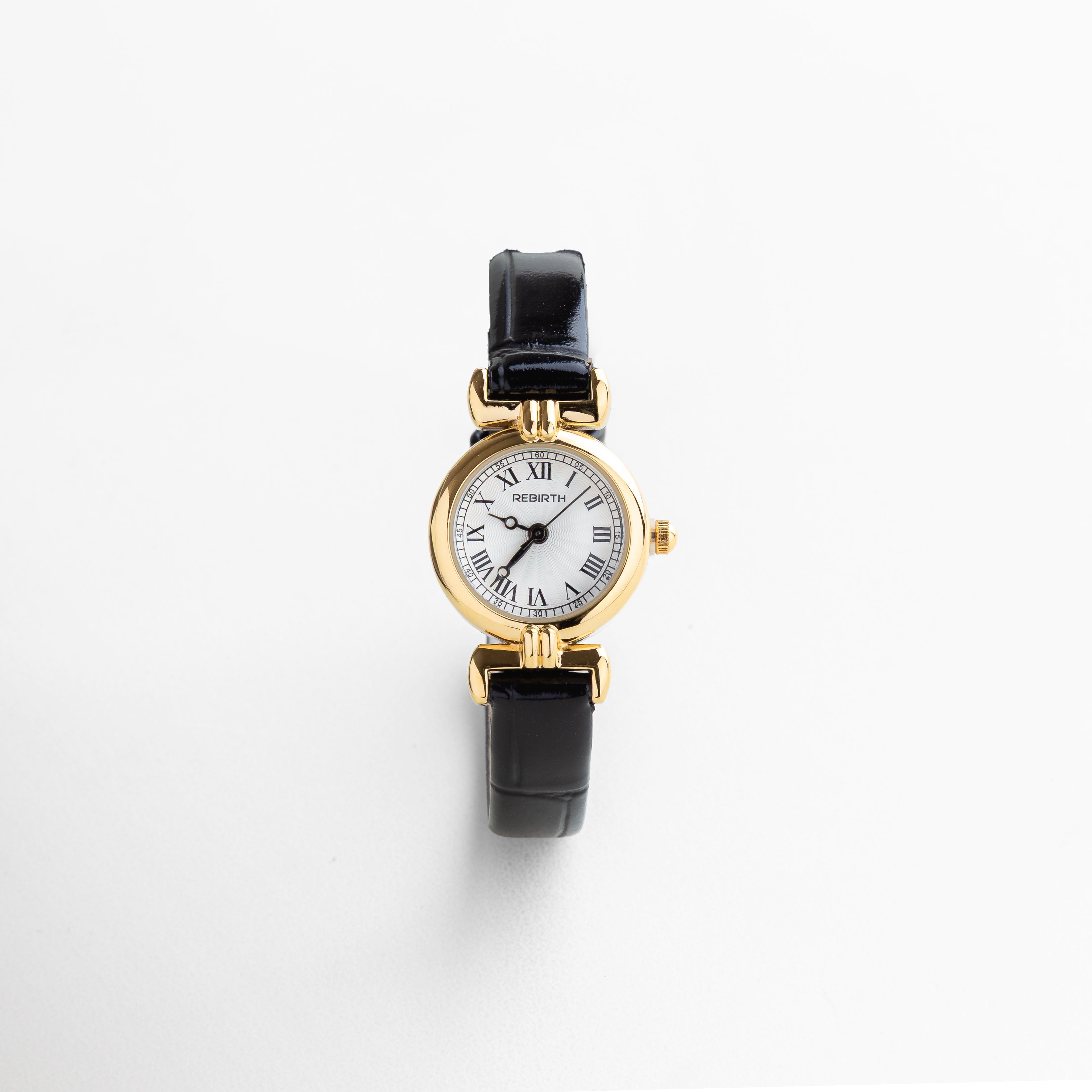 Detalle del reloj petite con vitrina dorada de 2 cm, mostrando su acabado brillante y diseño delicado. Close-up del reloj con correa de piel negra y caja en acero dorado, resaltando la textura suave del material.
 Zoom al rostro del reloj con carátula dorada, diseño femenino con estética pulida. Detalle del acabado en chapa de oro del reloj, combinado con correa negra delgada de 0.8 cm. Primer plano de la esfera dorada del reloj petite, con acabado espejo y diseño refinado.