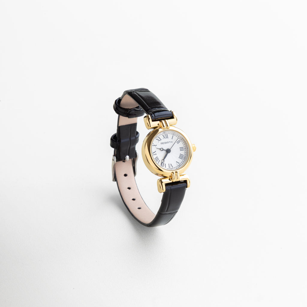 Reloj petite con correa negra y carátula dorada visto de frente, con diseño elegante y minimalista. Vista frontal del reloj femenino con vitrina circular de 2 cm y correa delgada en piel sintética. Reloj dorado con correa negra, diseño atemporal ideal para looks discretos y sofisticados. Primer plano del reloj en dorado y negro, con estilo clásico y moderno a la vez. Reloj de 22 cm con caja dorada y correa negra, visto desde el frente sobre fondo neutro.