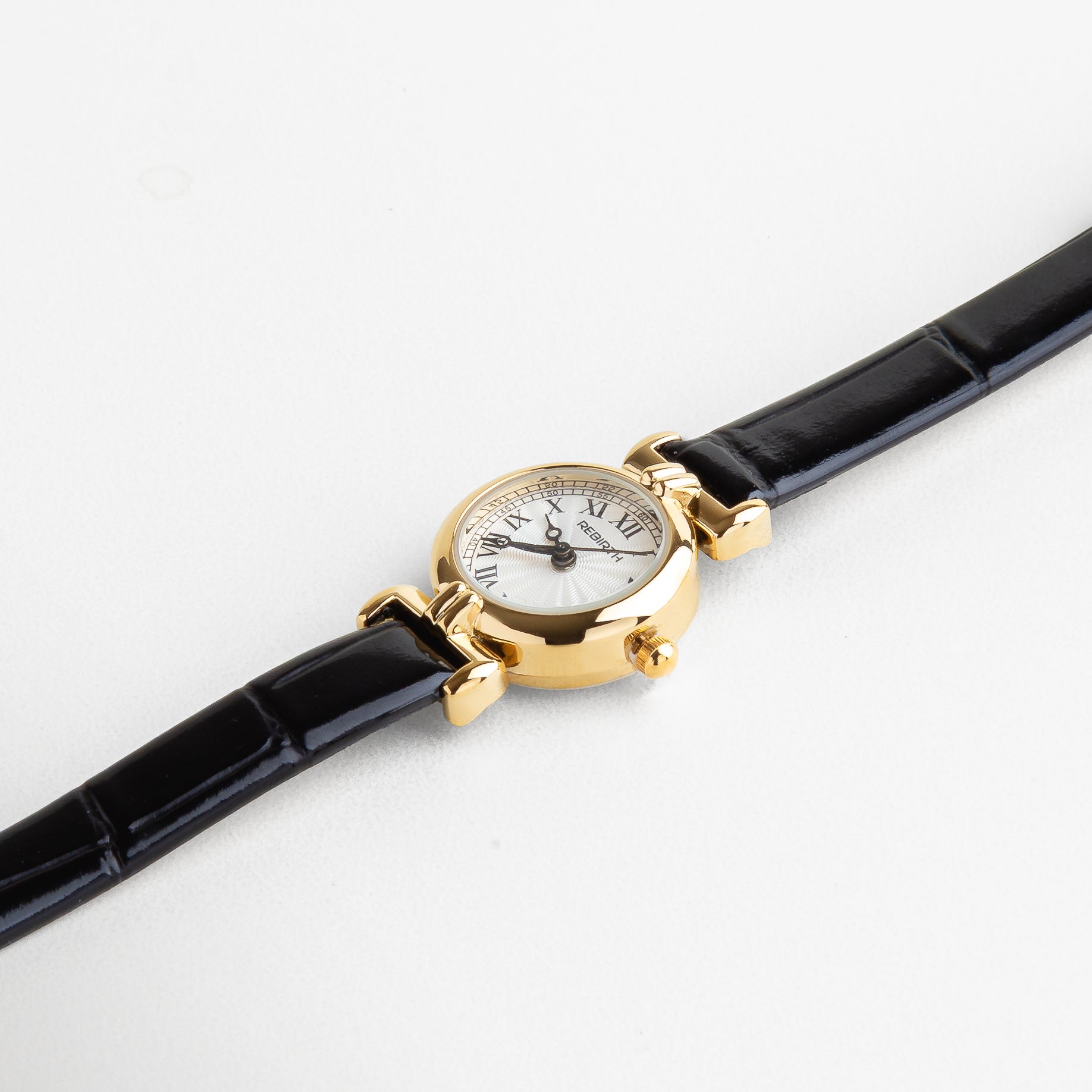 Reloj Petite visto desde el frente, con vitrina redonda dorada y correa negra delgada de piel sintética. Vista frontal del reloj elegante en formato mini, con caja dorada de 2 cm y diseño femenino y discreto. Primer plano del Reloj Petite con correa negra y esfera dorada, resaltando su sofisticación atemporal. Reloj dorado con correa negra, capturado desde el frente, ideal para un estilo clásico y versátil. Reloj mini dorado con diseño delicado y correa oscura, visto de frente sobre fondo ne