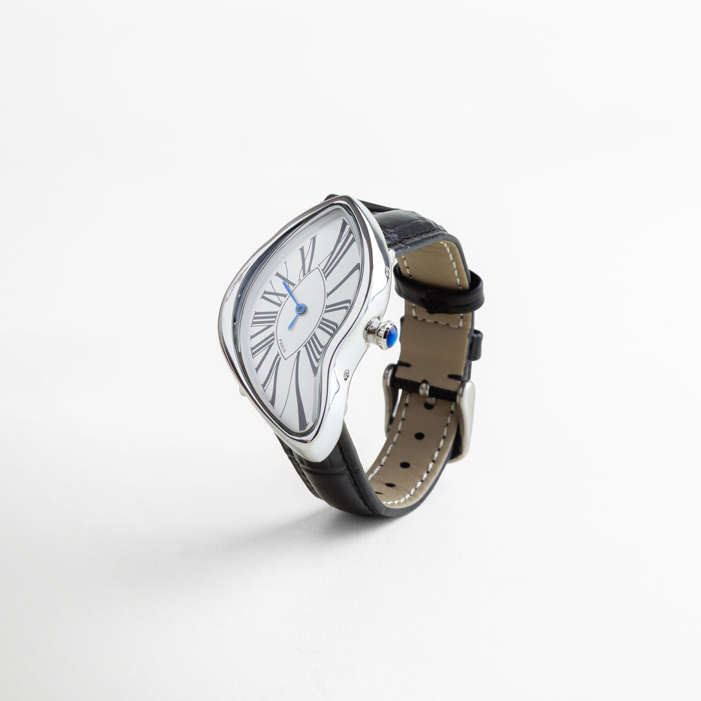 Reloj de acero de titanio con recubrimiento en oro 18K, dial blanco de 5 cm con números romanos en negro y manecillas azules, caja curvada de diseño artístico con correa negra en piel sintética, pieza llamativa y sofisticada.
