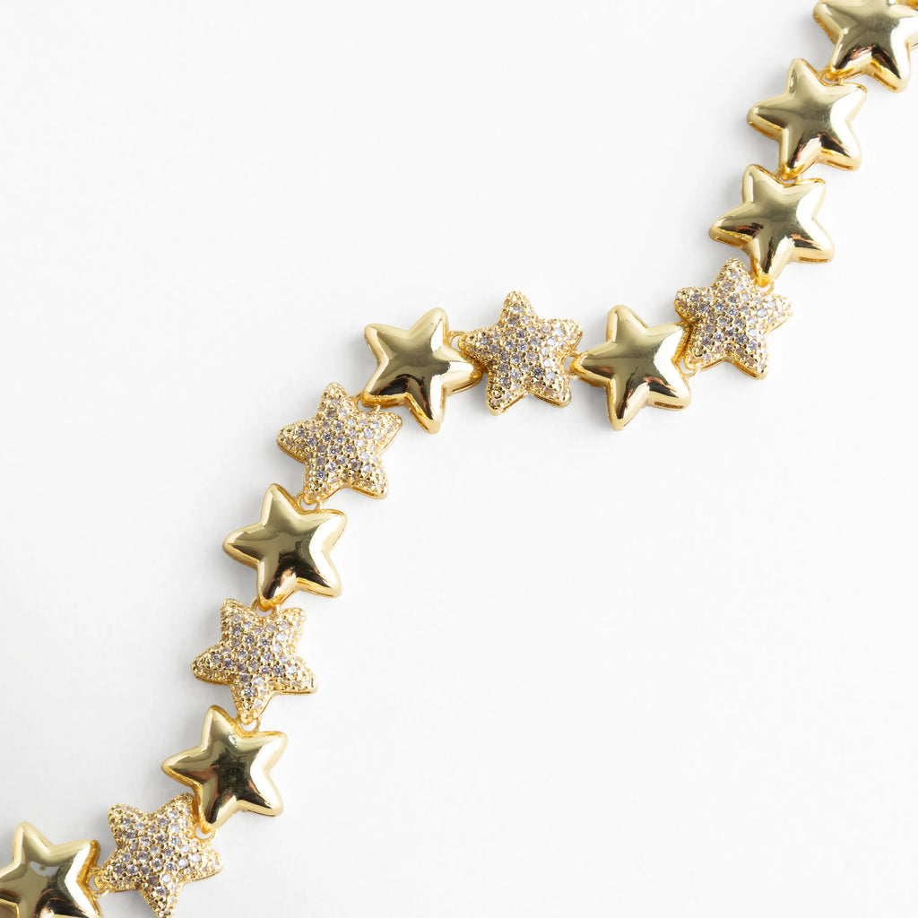 Pulsera dorada con estrellas alternadas entre acabado liso y brillantes incrustaciones de zirconias transparentes. El diseño resalta por su brillo celestial y la textura contrastante entre el metal pulido y las piedras relucientes, evocando la elegancia de un cielo iluminado por constelaciones.