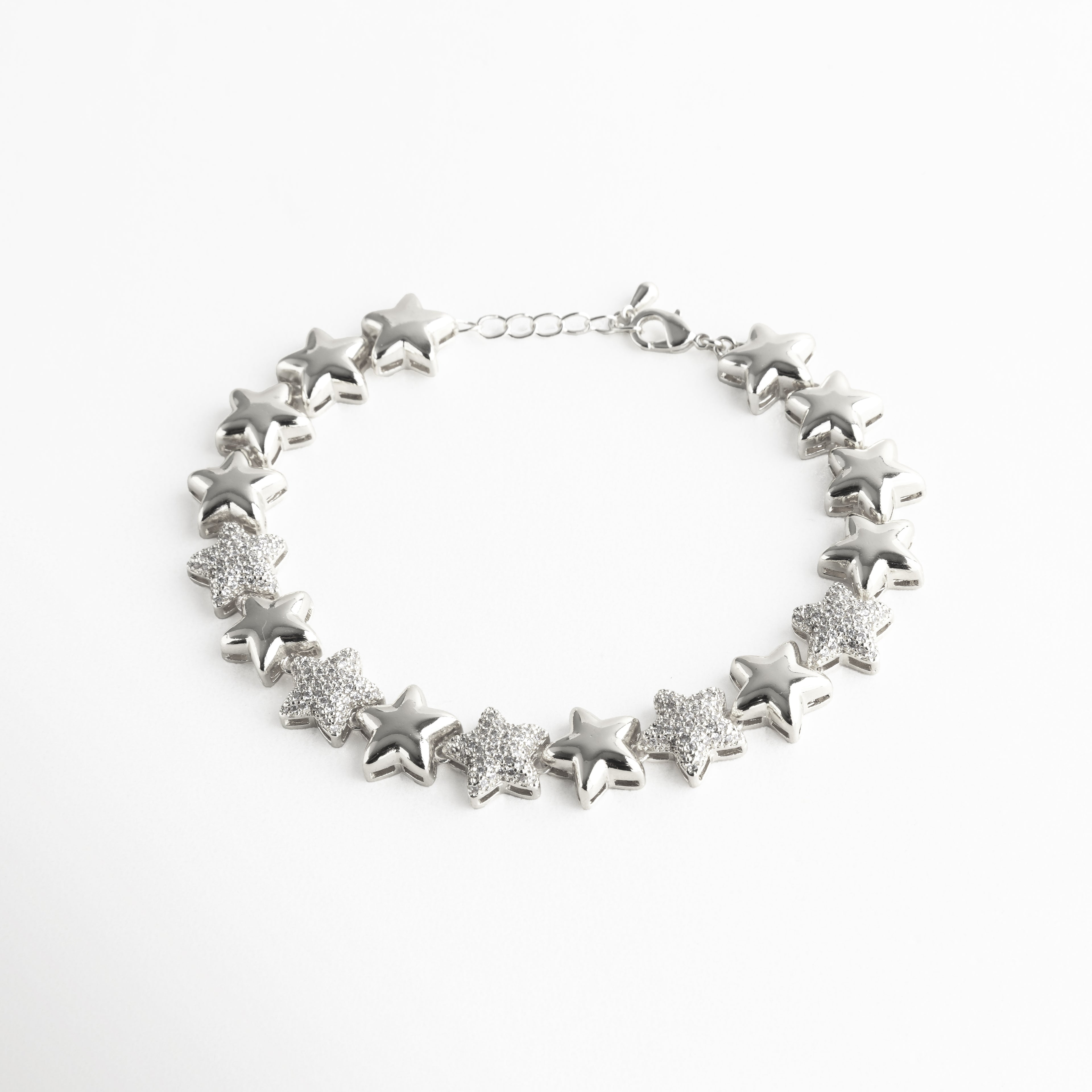 Pulsera plateada con estrellas alternadas entre acabado liso y brillantes incrustaciones de zirconias transparentes. El diseño resalta por su brillo celestial y la textura contrastante entre el metal pulido y las piedras relucientes, evocando la elegancia de un cielo iluminado por constelaciones.