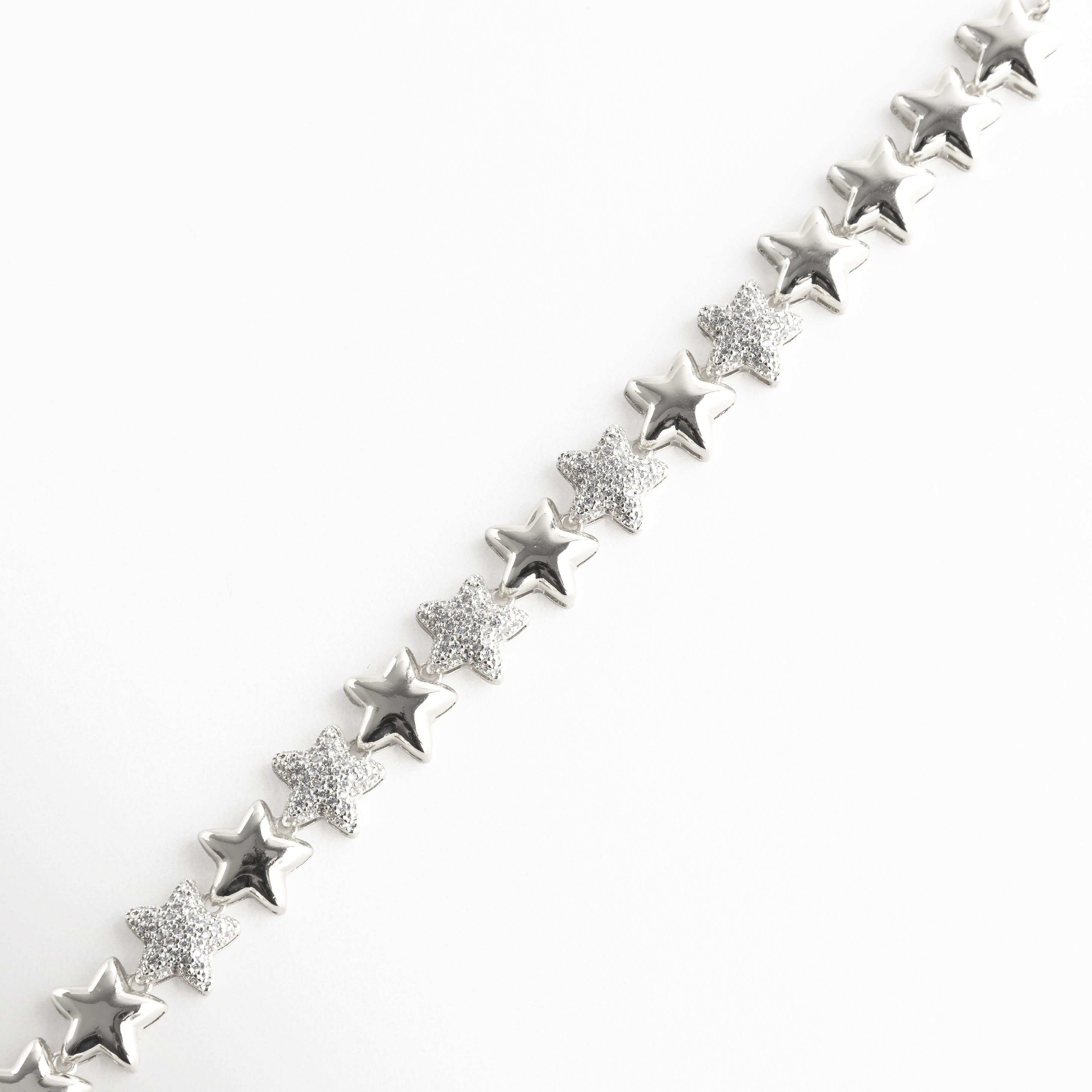 Pulsera plateada compuesta por estrellas en relieve, intercaladas con zirconias que aportan un brillo sutil y sofisticado. Su estructura articulada permite que se adapte con suavidad a la muñeca, ideal para elevar cualquier look con un toque de luz y delicadeza.