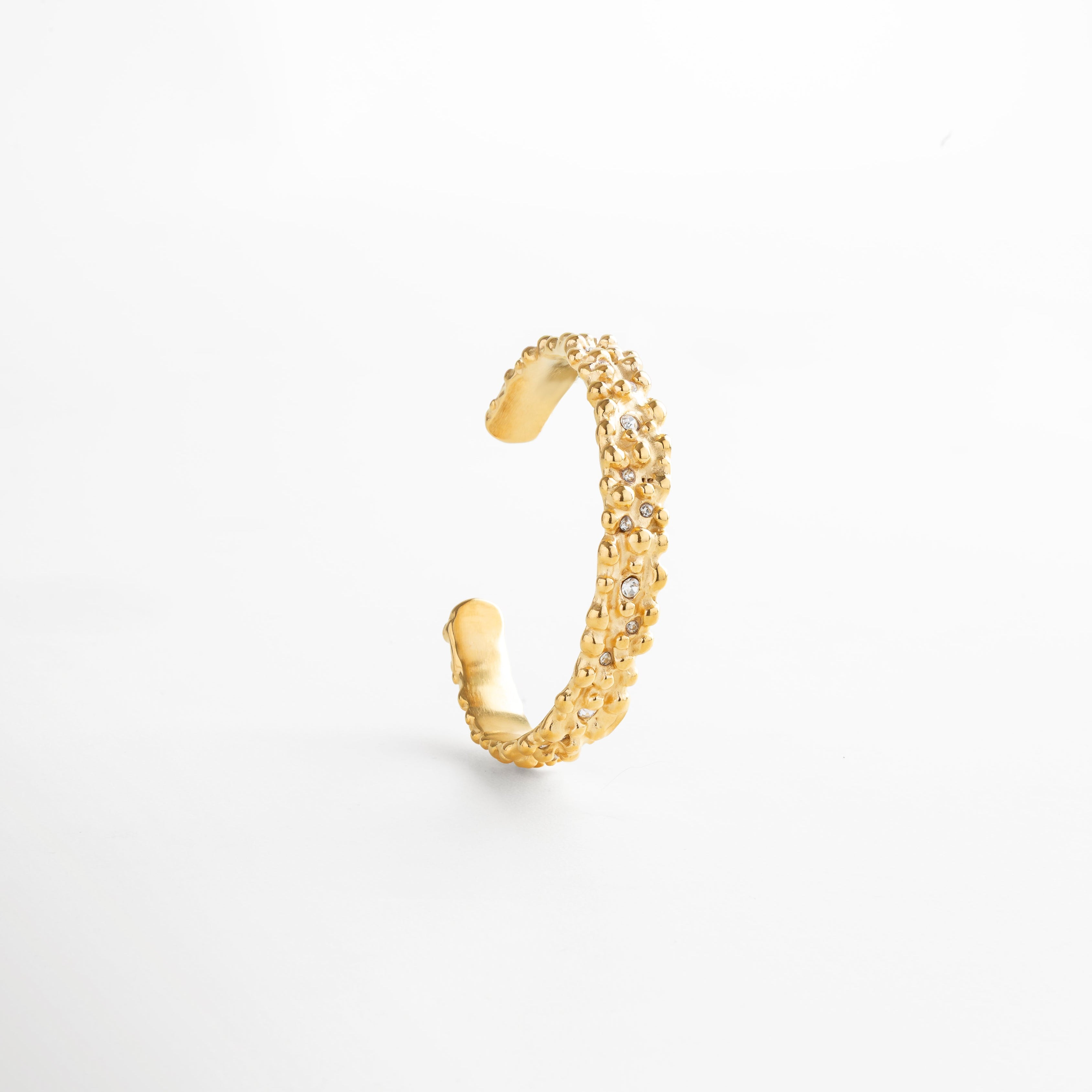 Pulsera abierta dorada con textura orgánica y zirconias brillantes, diseño moderno en acero inoxidable con baño de oro 18K, joya elegante y versátil para looks sofisticados.