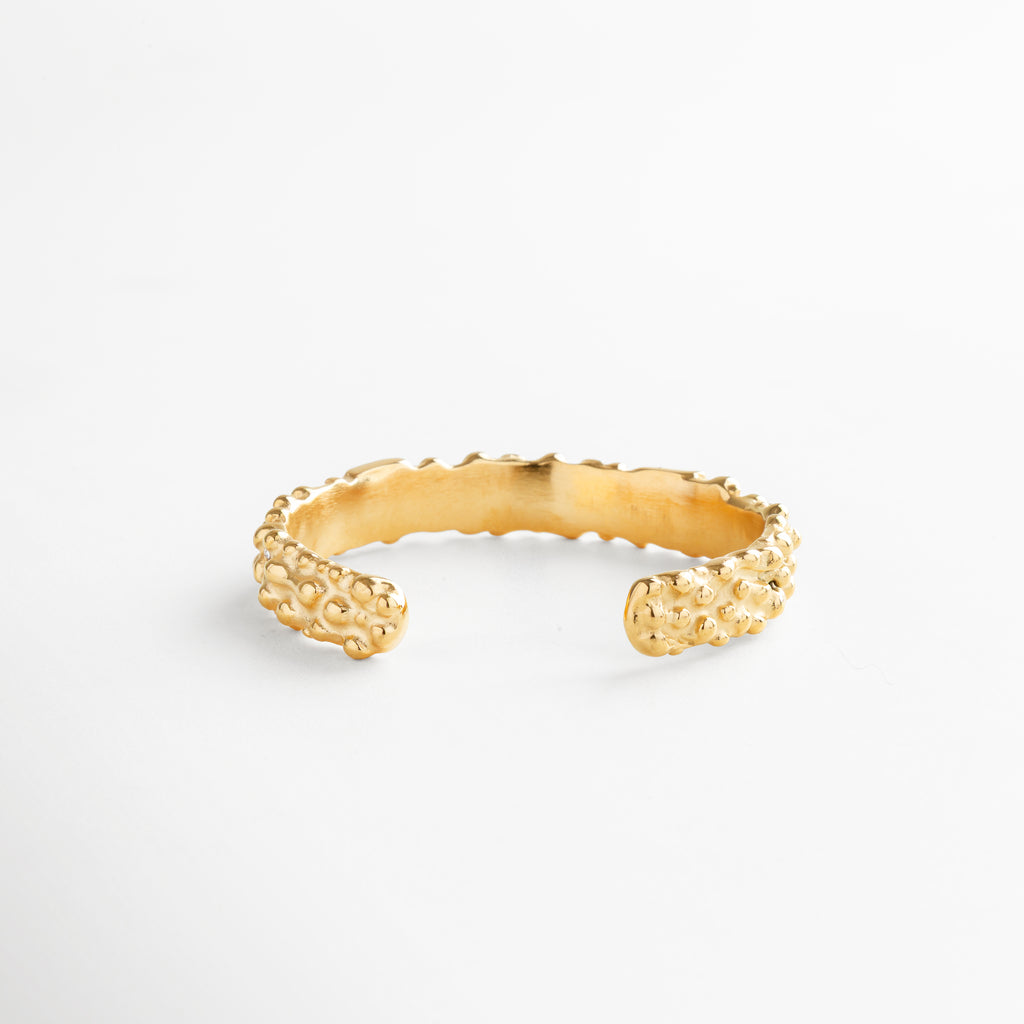 Pulsera abierta dorada con acabado martillado y textura orgánica, diseño minimalista en acero inoxidable con baño en oro 18K, pieza versátil y moderna sin cierres.