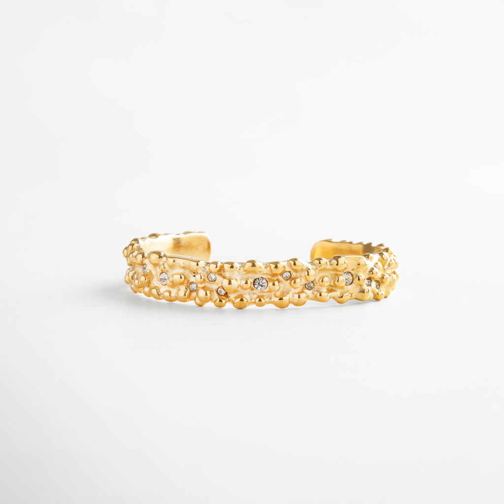 Pulsera rígida dorada con incrustaciones de zirconias, detalle texturizado en oro 18K, accesorio de lujo atemporal para realzar cualquier outfit con elegancia.