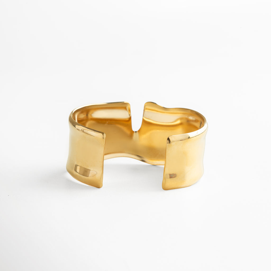 Pulsera abierta dorada con diseño ajustable, acabado pulido en oro 18K, joya bold y contemporánea que combina minimalismo con sofisticación.