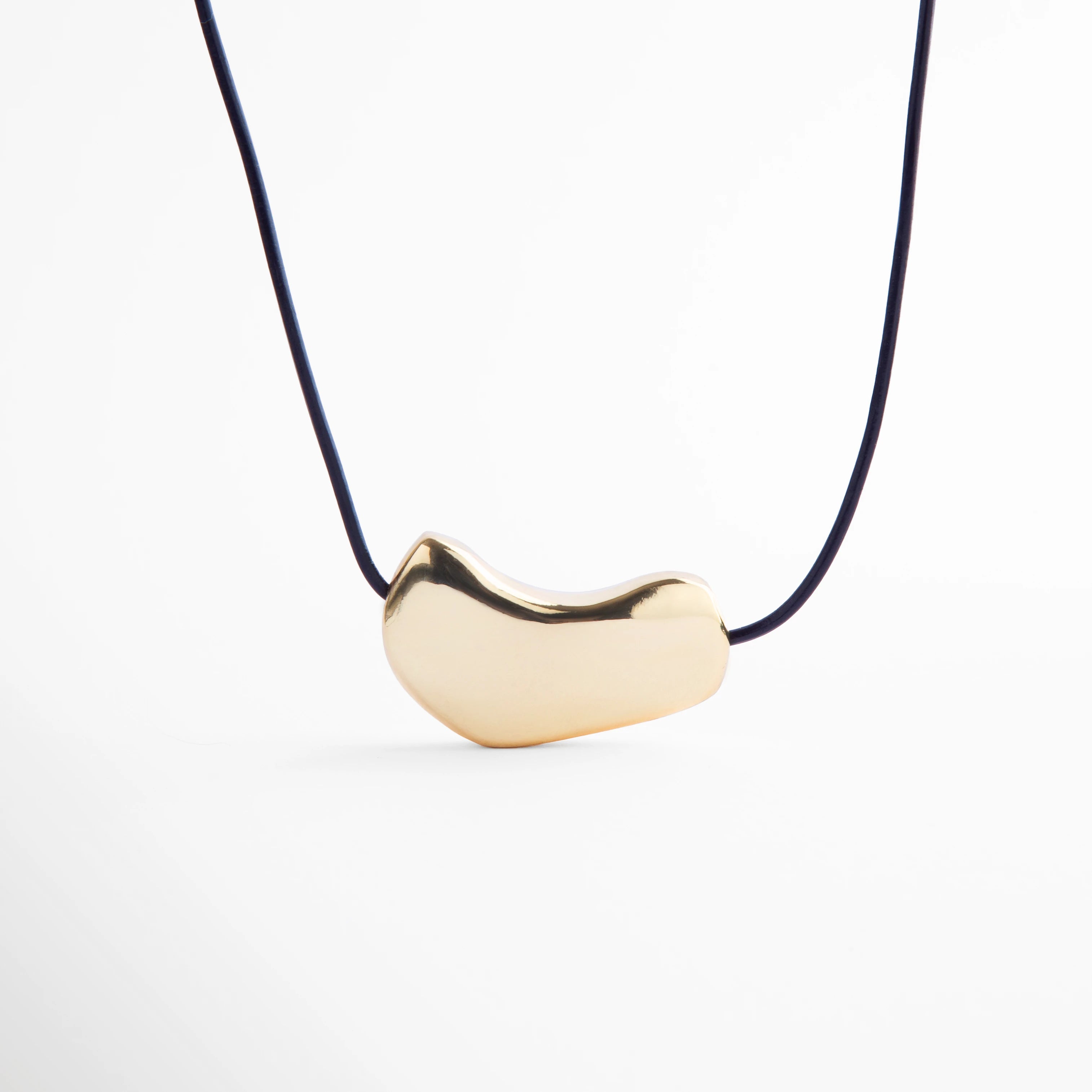 Collar dorado minimalista con dije metálico de forma orgánica sobre cordón negro, joya moderna de acabado pulido que resalta por su elegancia y estilo contemporáneo.