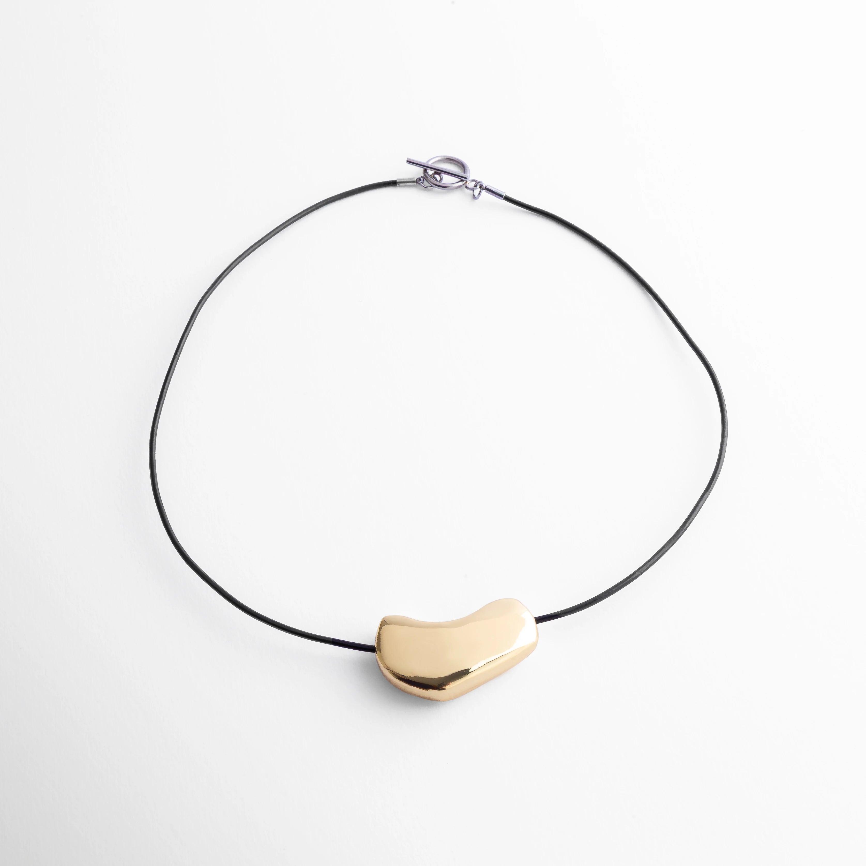 Collar contemporáneo dorado con pieza escultórica sobre cordón negro, diseño minimalista y sofisticado, ideal para quienes buscan un toque moderno y atemporal.