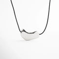 Collar corto plateado con dije metálico orgánico de acabado brillante sobre cordón negro, diseño moderno y minimalista ideal para looks elegantes o casuales.
