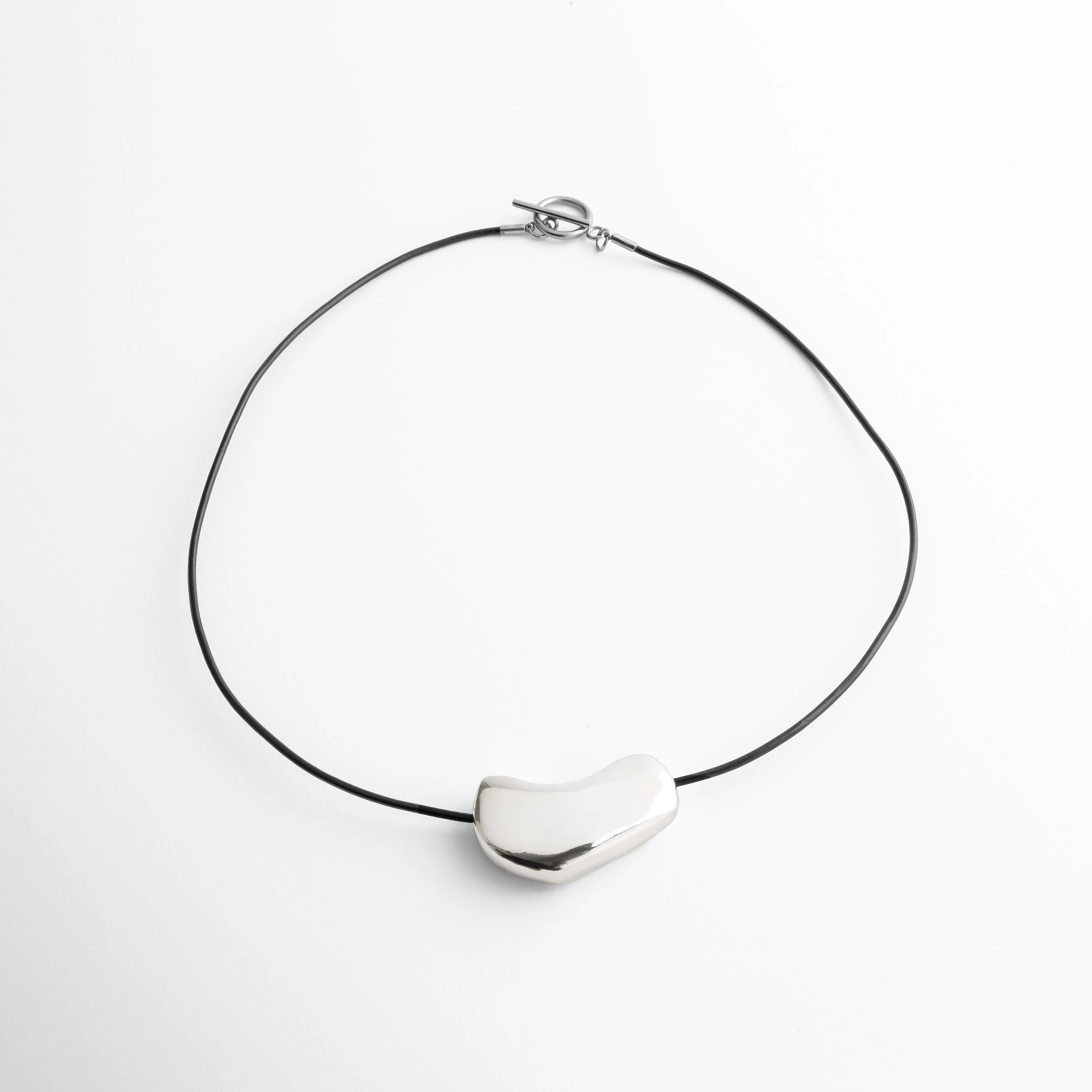 Collar contemporáneo plateado con pieza escultórica sobre cordón negro, estilo minimalista inspirado en formas naturales, perfecto para destacar con discreción.