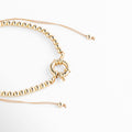 Pulsera dorada ajustable con esferas metálicas brillantes y cierre circular central. Diseño elegante y versátil ideal para combinar con cualquier look, perfecta para uso diario o eventos especiales.