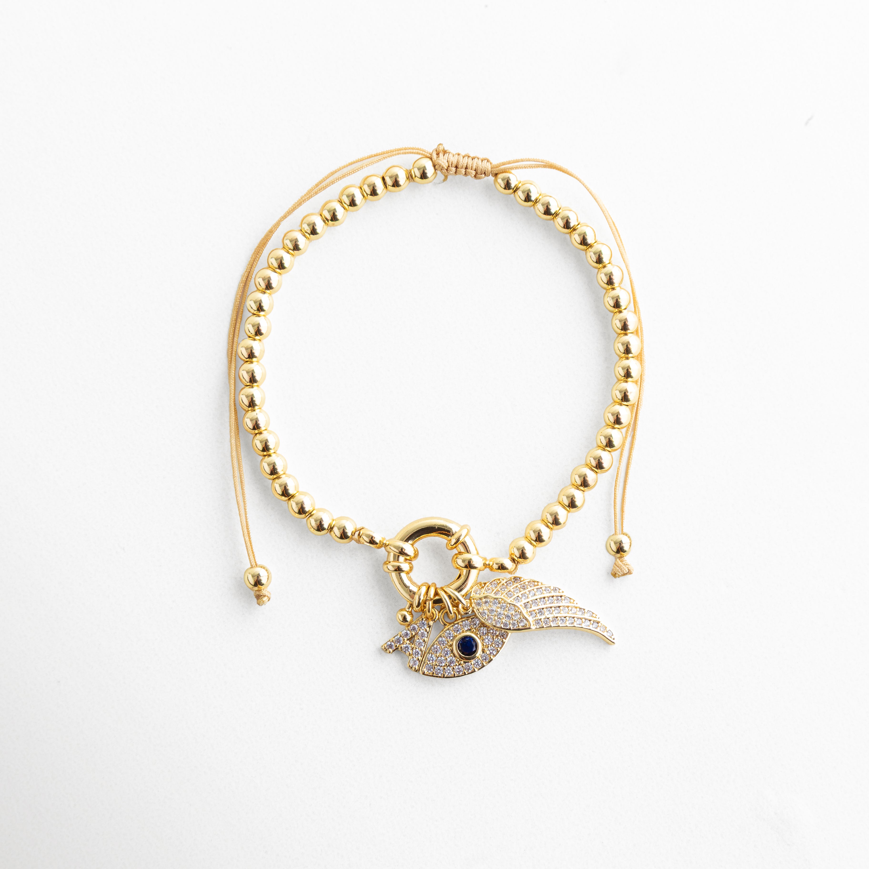 Pulsera dorada con esferas metálicas y dije en forma de ojo turco con alas decoradas con circonias brillantes. Accesorio llamativo y sofisticado que añade un toque de protección y estilo a tu outfit.