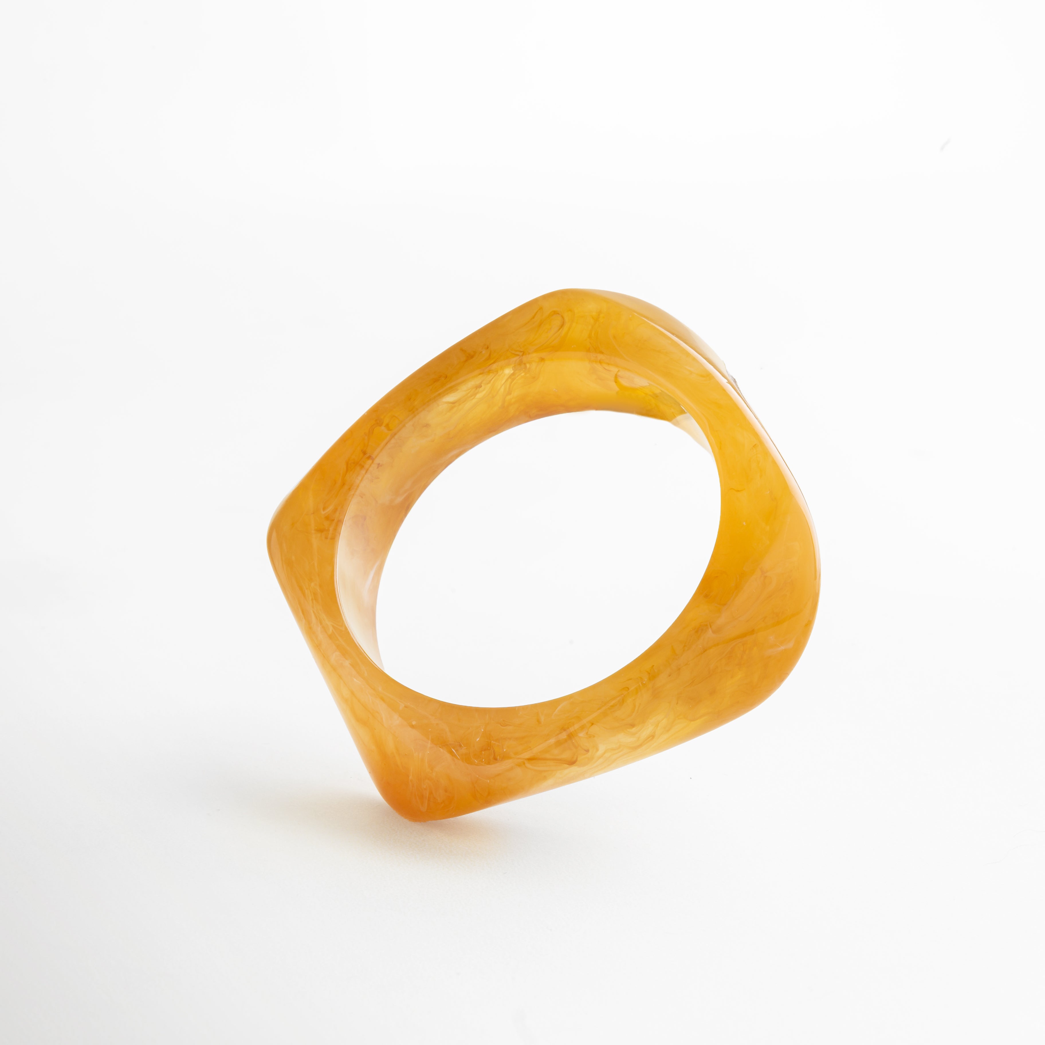 Pulsera geométrica de resina en tono ámbar cálido, diseño escultural con acabado marmoleado brillante, pieza moderna y sofisticada.