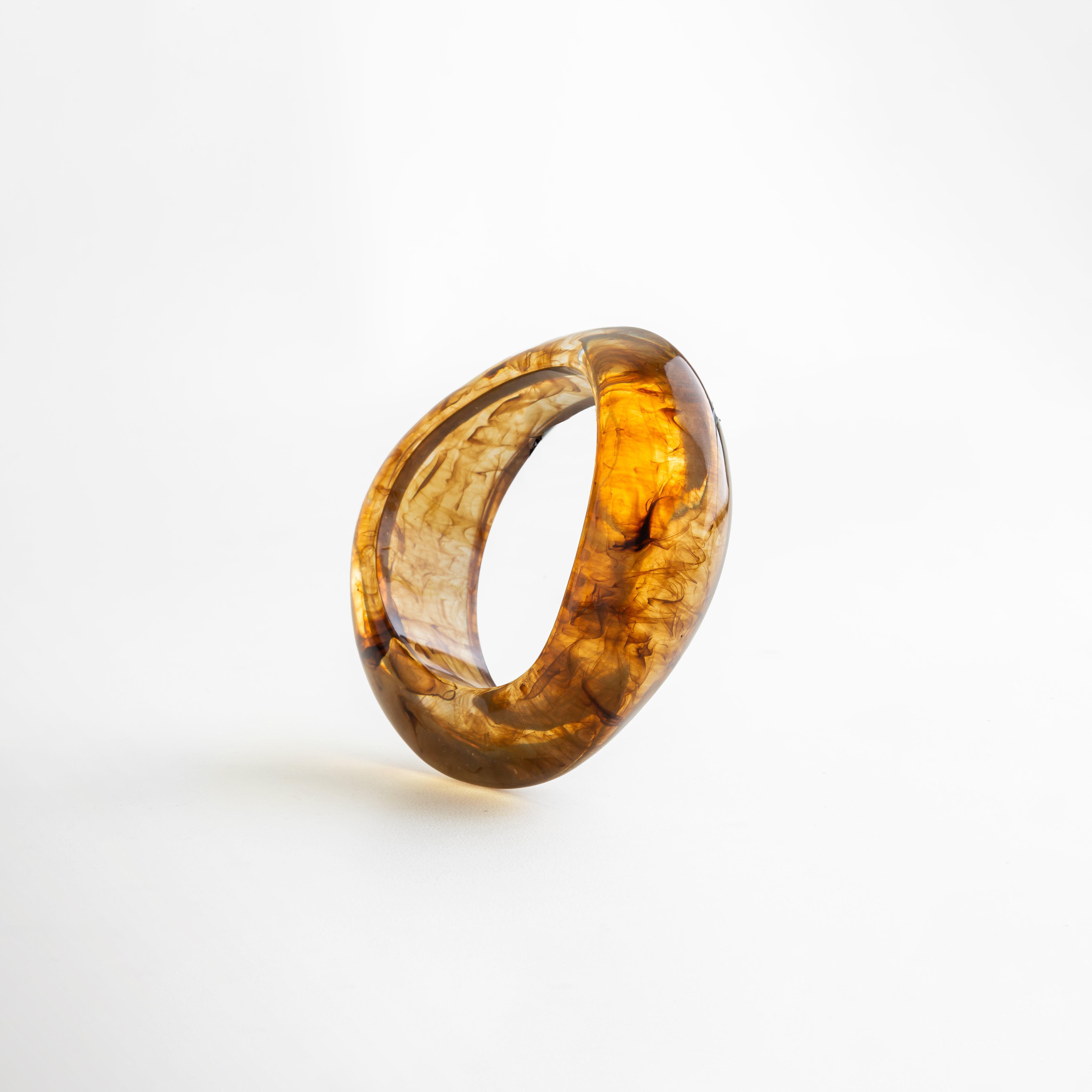 Pulsera bold de resina en tono ámbar con acabado marmoleado, diseño escultural y moderno de líneas orgánicas, ideal como accesorio statement.