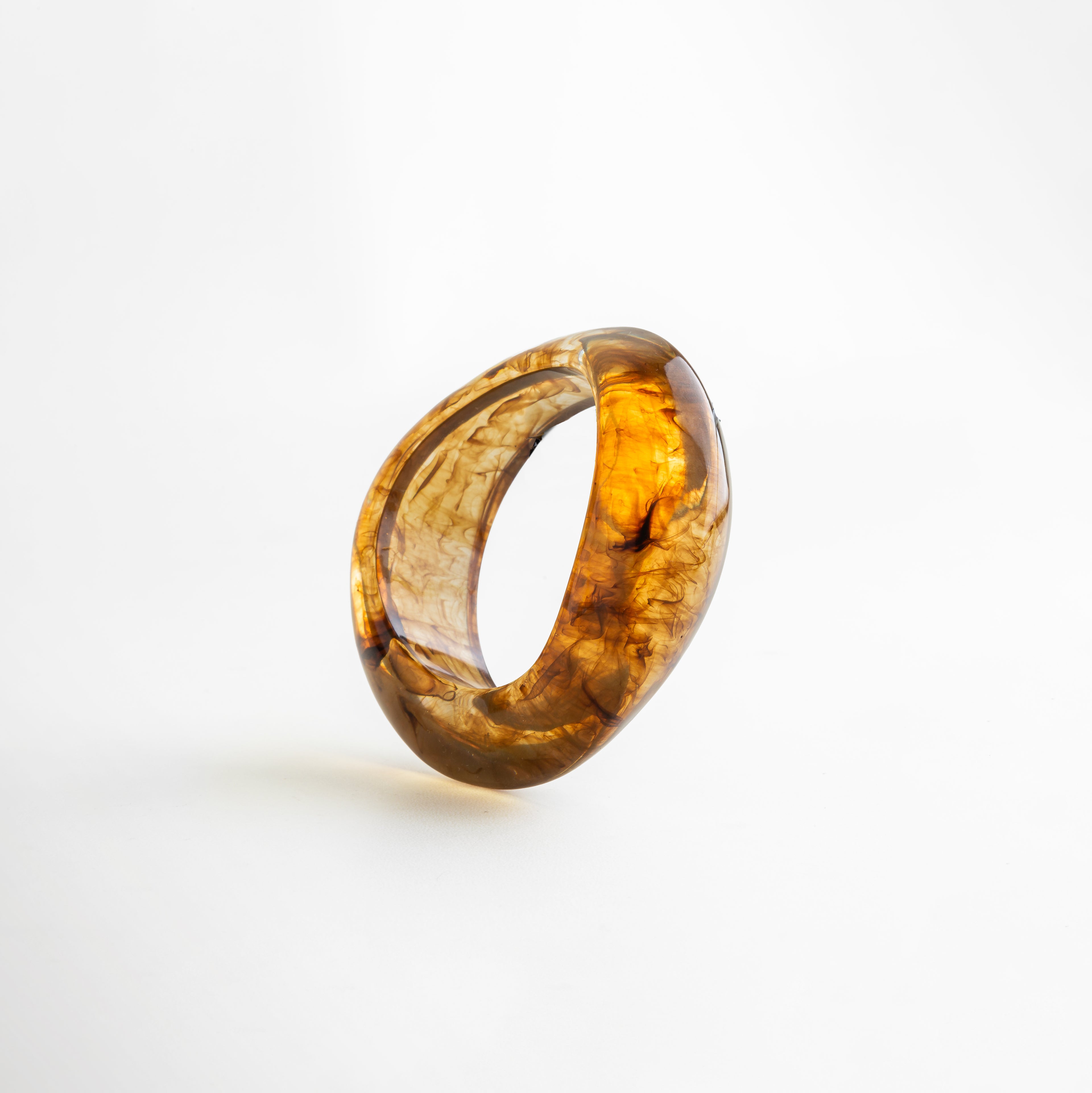 Pulsera bold de resina en tono ámbar con acabado marmoleado, diseño escultural y moderno de líneas orgánicas, ideal como accesorio statement.