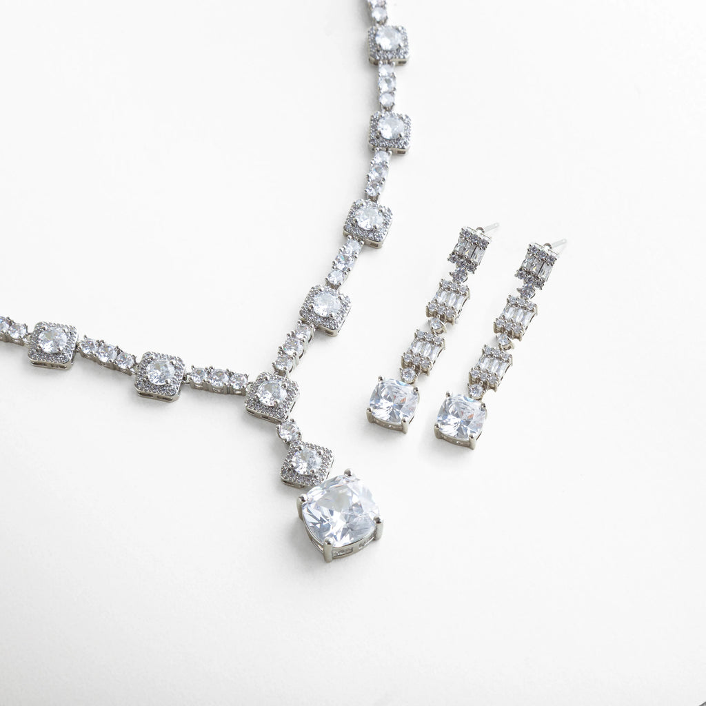 Vista del set de collar y aretes con zirconias transparentes, donde el reflejo del metal plateado resalta el resplandor cristalino de cada piedra. La composición combina elegancia moderna con un aire clásico que complementa cualquier look formal.