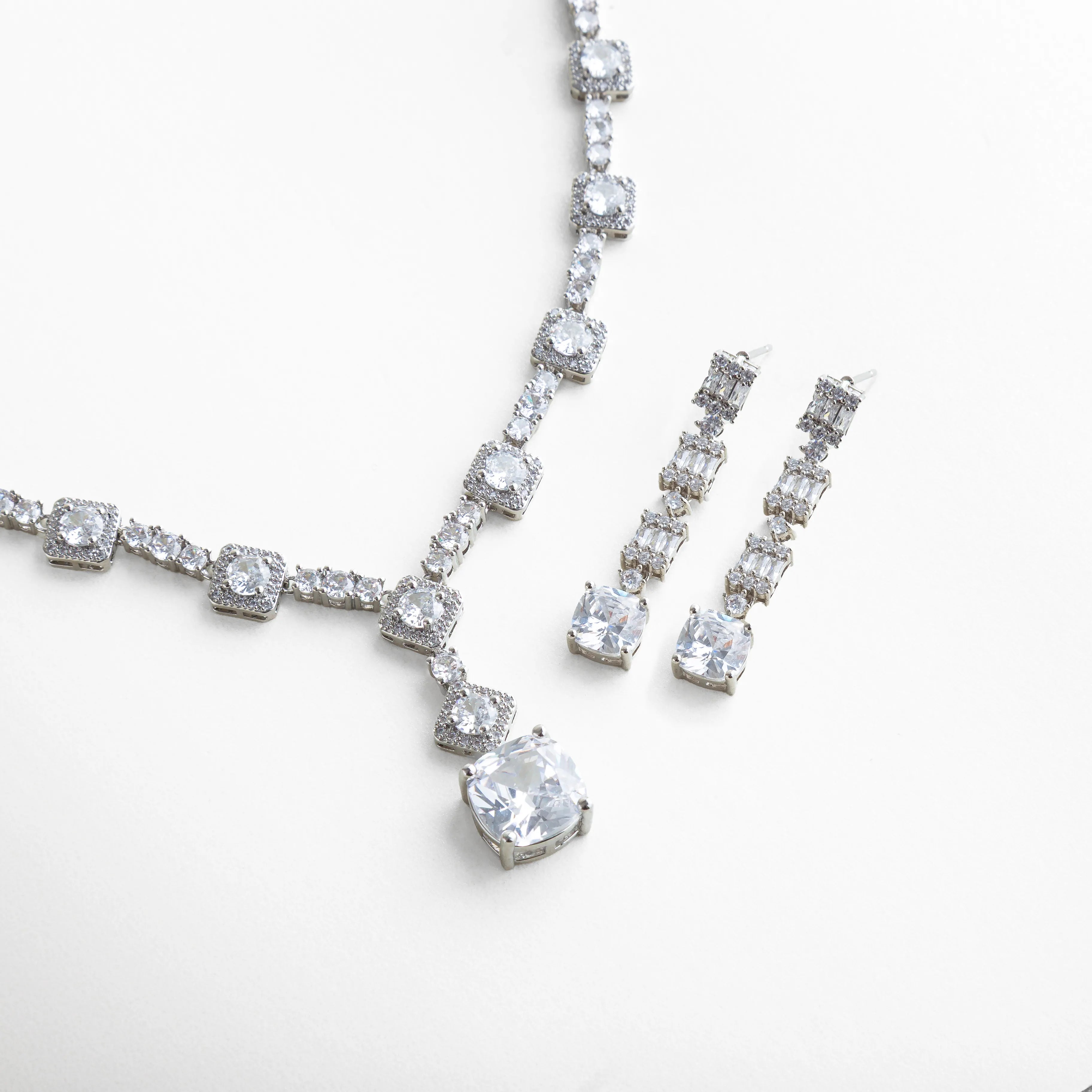 Vista del set de collar y aretes con zirconias transparentes, donde el reflejo del metal plateado resalta el resplandor cristalino de cada piedra. La composición combina elegancia moderna con un aire clásico que complementa cualquier look formal.