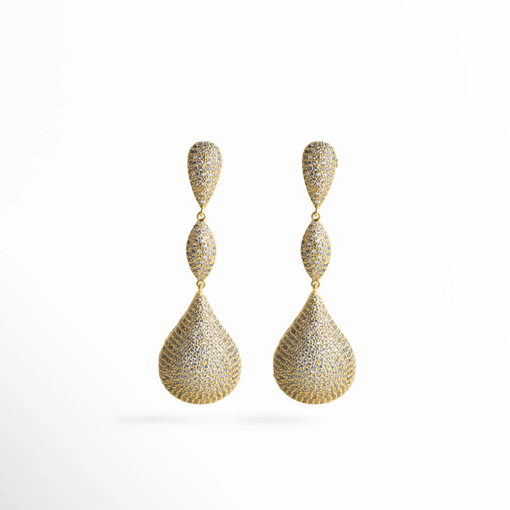 Aretes dorados largos con zirconias incrustadas, diseño elegante en forma de gota triple que refleja brillo y sofisticación.