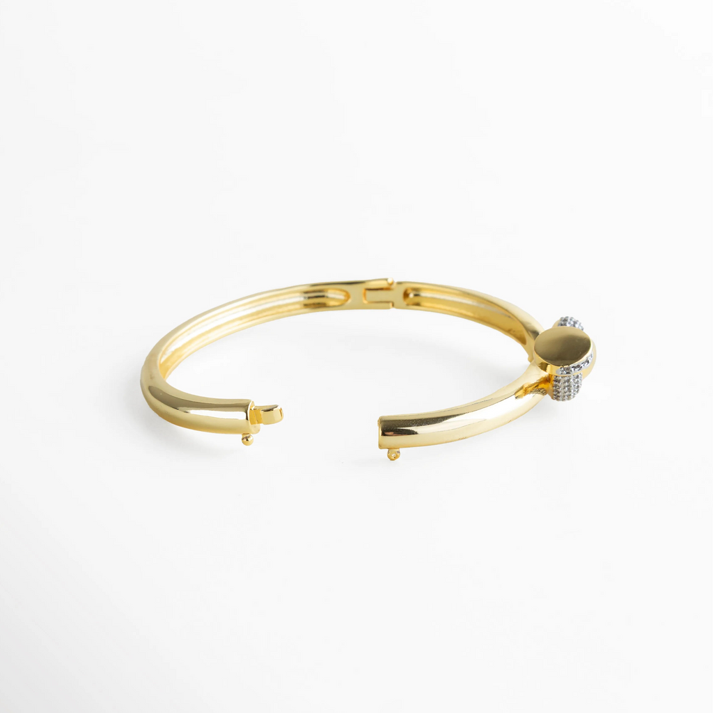 Pulsera rígida dorada con sistema de apertura invisible y broche seguro, destacando su estructura sólida y el diseño fluido del nudo. La toma enfatiza su practicidad sin perder la esencia lujosa de la pieza, perfecta para uso diario o eventos especiales.