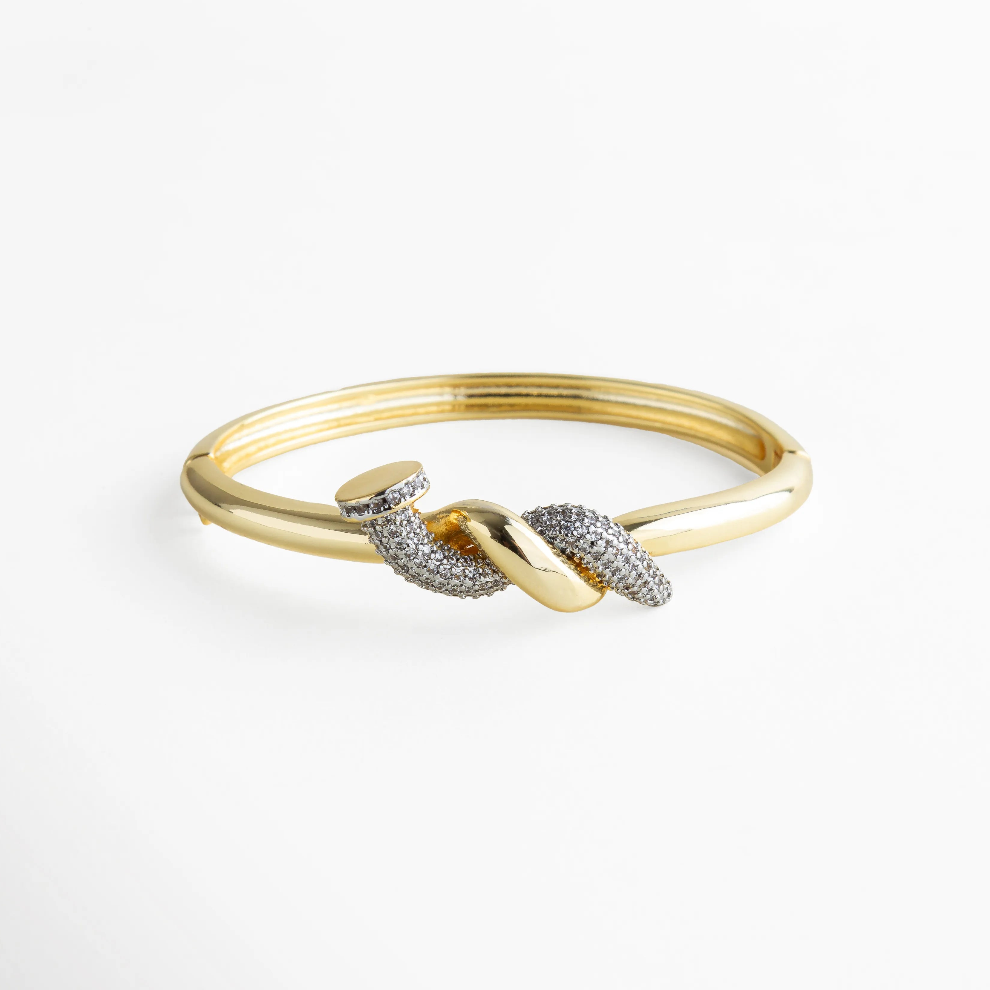 Pulsera dorada tipo brazalete con detalle de nudo central adornado con zirconias transparentes incrustadas. La mezcla entre el brillo del metal y el resplandor de las piedras crea un efecto elegante y sofisticado, ideal para elevar cualquier look con un toque moderno y refinado.