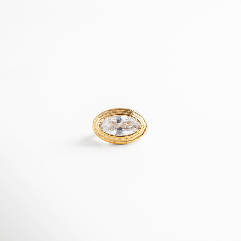 Anillo dorado de acero con zirconia ovalada blanca, diseño elegante y brillante sobre fondo blanco.