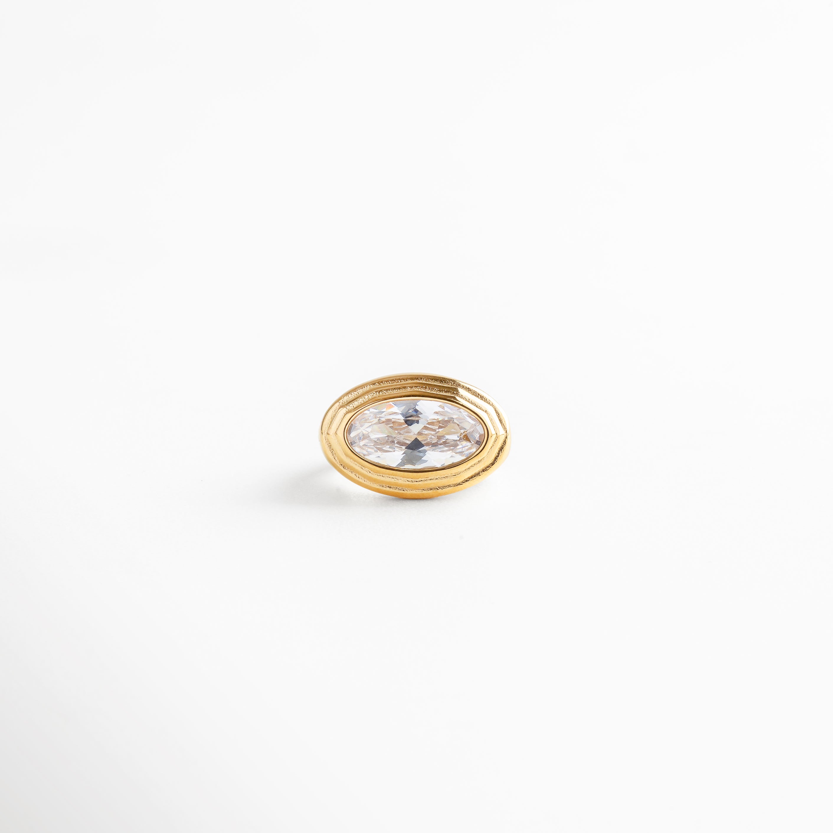 Anillo dorado de acero con zirconia ovalada blanca, diseño elegante y brillante sobre fondo blanco.
