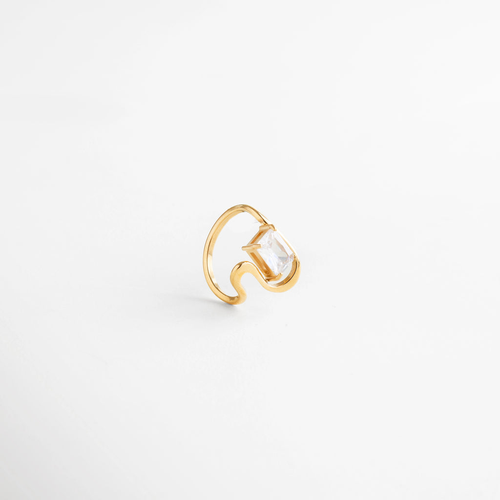 Anillo dorado con piedra transparente en montaje abierto, diseño contemporáneo, Detalle lateral de anillo dorado con zirconia cuadrada, estilo moderno.