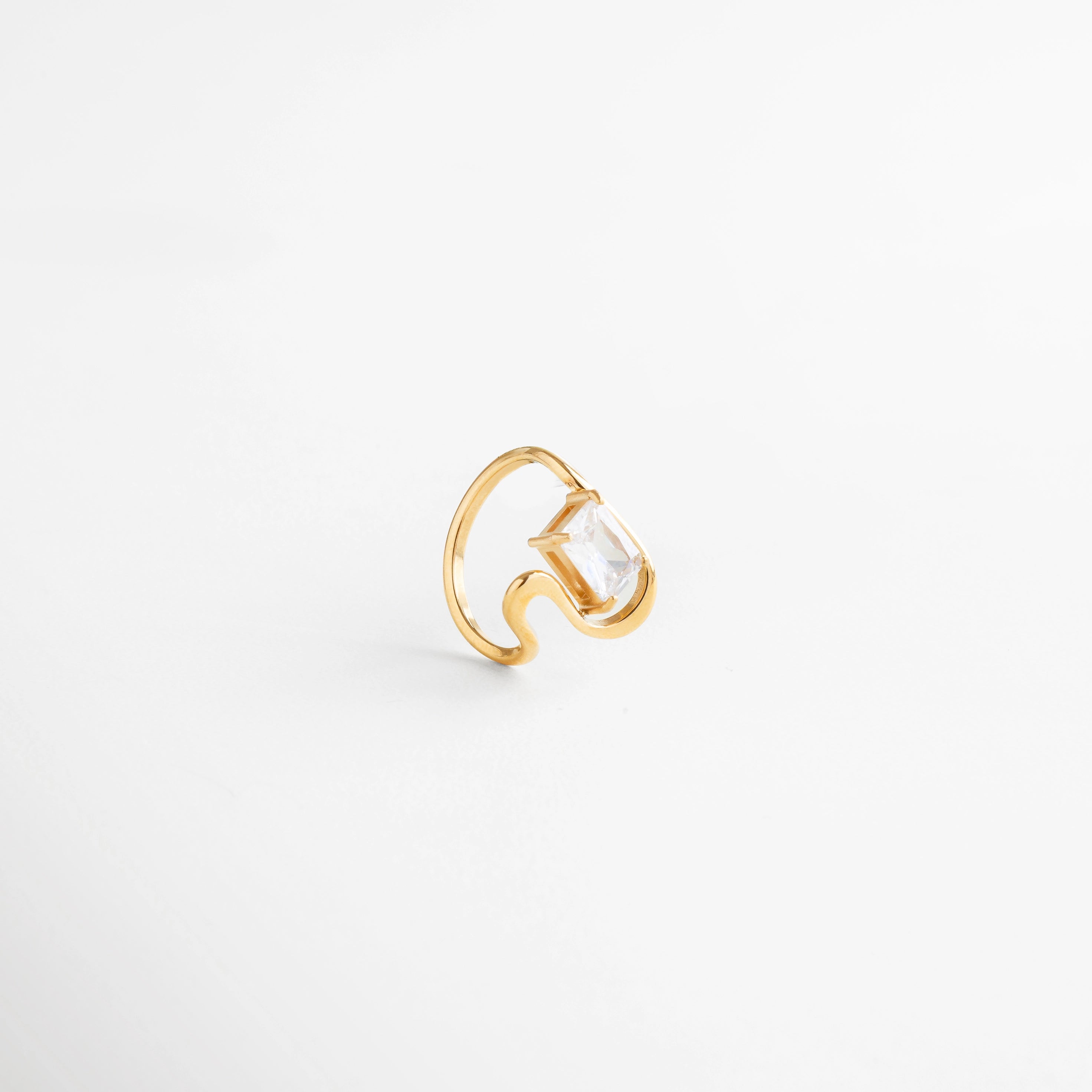 Anillo dorado con piedra transparente en montaje abierto, diseño contemporáneo, Detalle lateral de anillo dorado con zirconia cuadrada, estilo moderno.