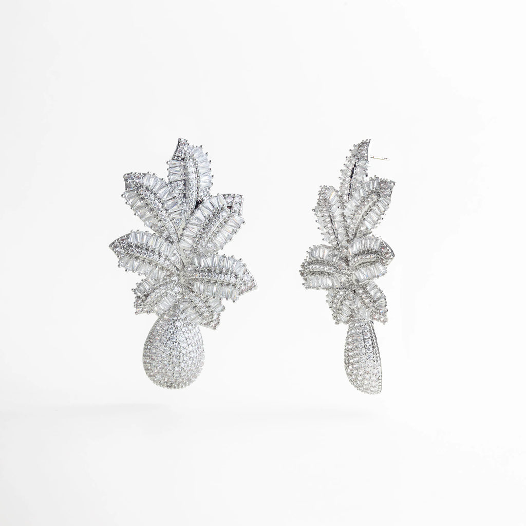 detalle de textura brillante en aretes plateados, aretes plateados con acabado luminoso y facetado, joyería statement plateada con trabajo detallado, aretes plateados con inspiración natural, detalle de hojas metálicas en aretes plateados, aretes plateados con textura fina y reflejo de luz