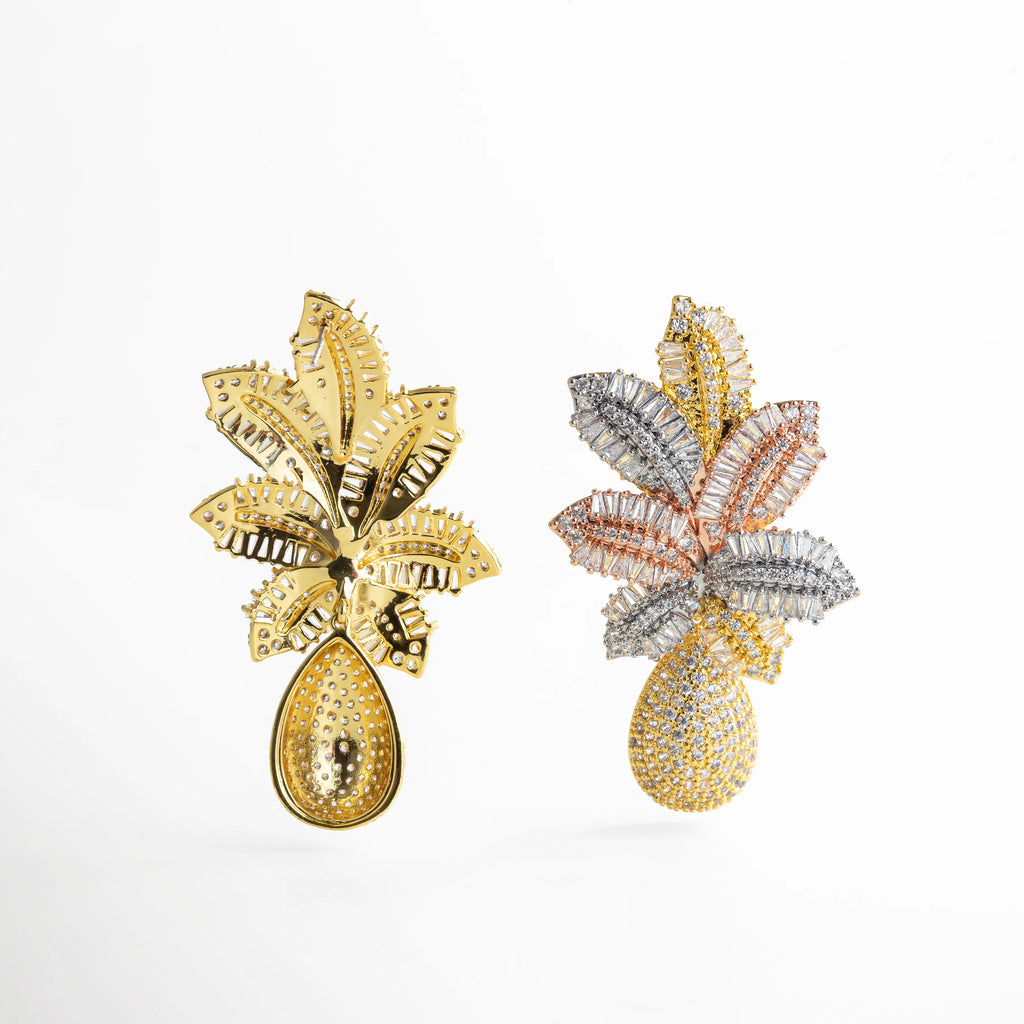 Vista trasera de aretes dorados largos con diseño de hojas y gota multicolor con cristales brillantes; fondo blanco.