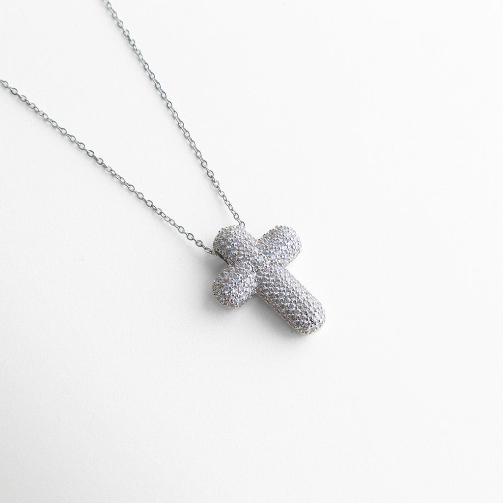 detalle de cruz con zirconias pavé en collar plateado, colgante de cruz con piedras brillantes en primer plano, collar con dije de cruz texturizado con zirconias, detalle de joyería con cruz luminosa, colgante religioso moderno con zirconias