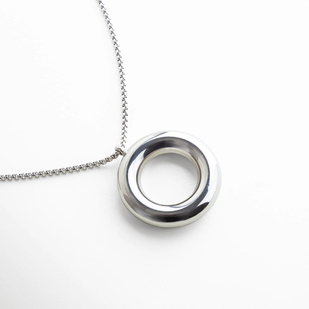 Collar plateado con dije circular de superficie lisa y alto brillo, suspendido en una cadena delgada. Su diseño escultural evoca elegancia discreta y un estilo moderno que combina con looks minimalistas o formales.