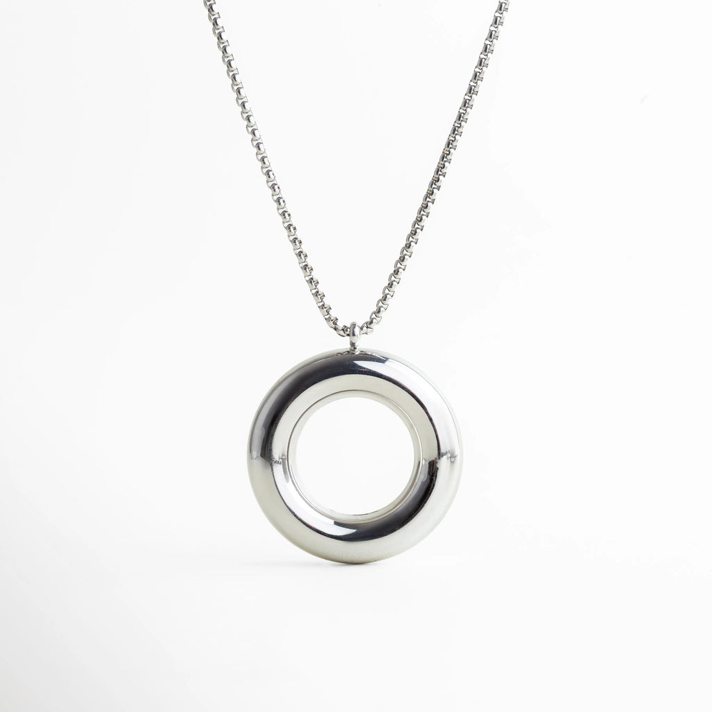 Collar plateado con dije circular suspendido, capturado en caída natural. Su forma refleja equilibrio y modernidad, perfecta para elevar atuendos sobrios con un toque artístico y contemporáneo.