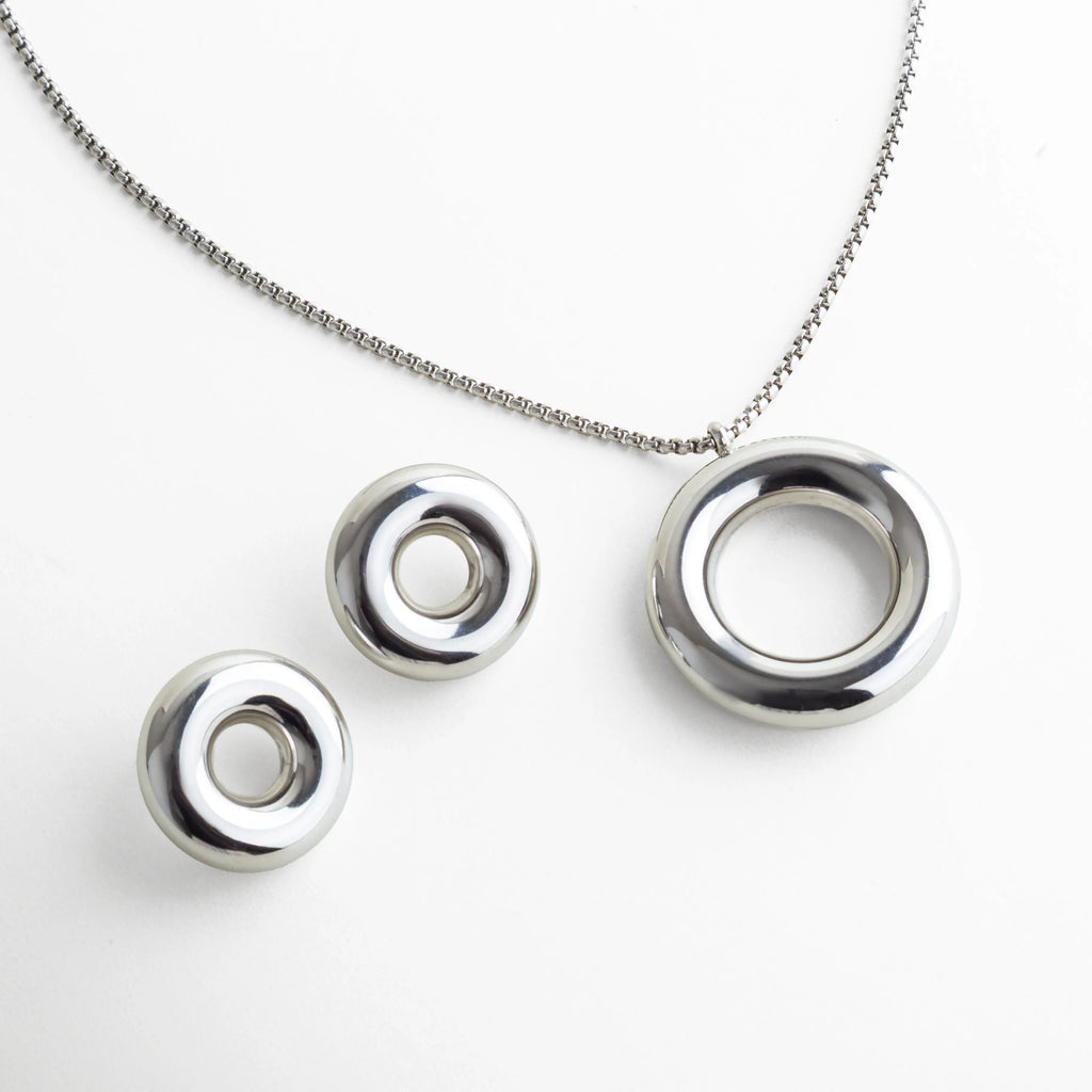 Set plateado minimalista compuesto por un collar y un par de aretes circulares de acabado pulido espejo. El diseño geométrico y la silueta redondeada aportan un aire moderno y arquitectónico, ideal para quienes prefieren piezas contemporáneas y atemporales.