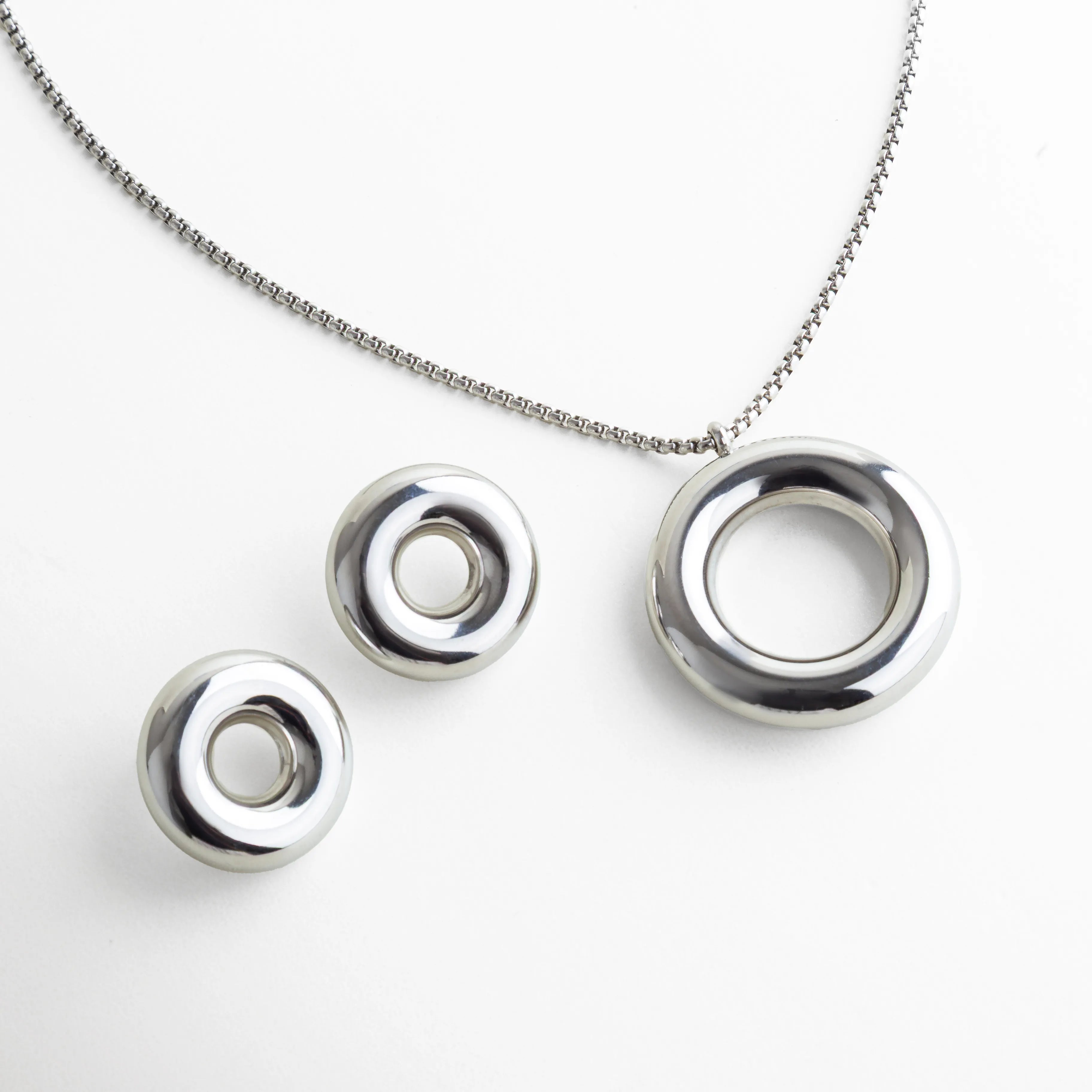Set plateado minimalista compuesto por un collar y un par de aretes circulares de acabado pulido espejo. El diseño geométrico y la silueta redondeada aportan un aire moderno y arquitectónico, ideal para quienes prefieren piezas contemporáneas y atemporales.