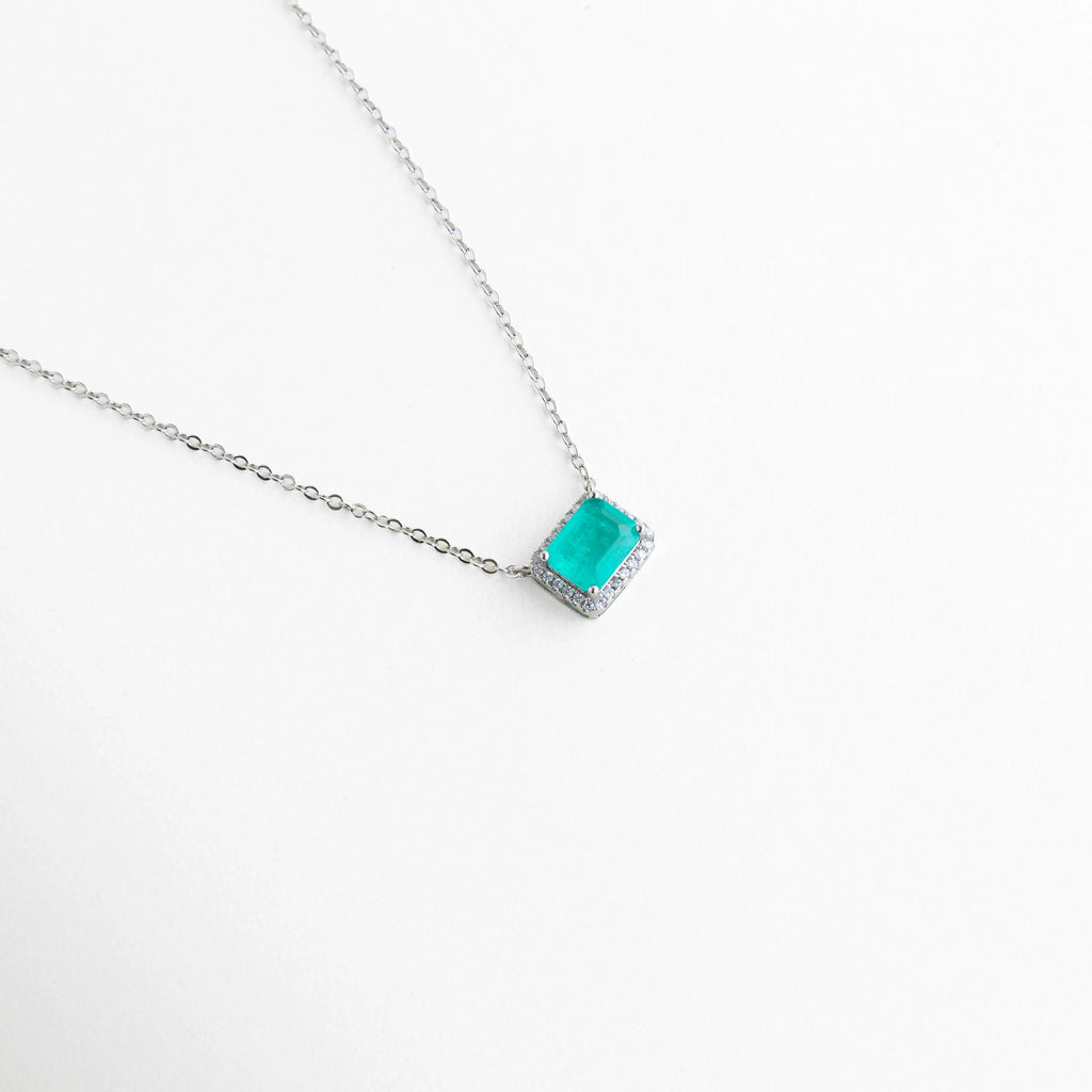 Dije de 1 cm color verde esmeralda montado en cadena de cobre enchapada, Collar delicado con piedra rectangular y halo de luz en acabado plateado, Vista en ángulo de joyería elegante con piedra verde para eventos especiales, Diseño moderno de collar con piedra esmeralda y marco de brillantes, Gargantilla con dije geométrico verde y recubrimiento de oro blanco 18K.