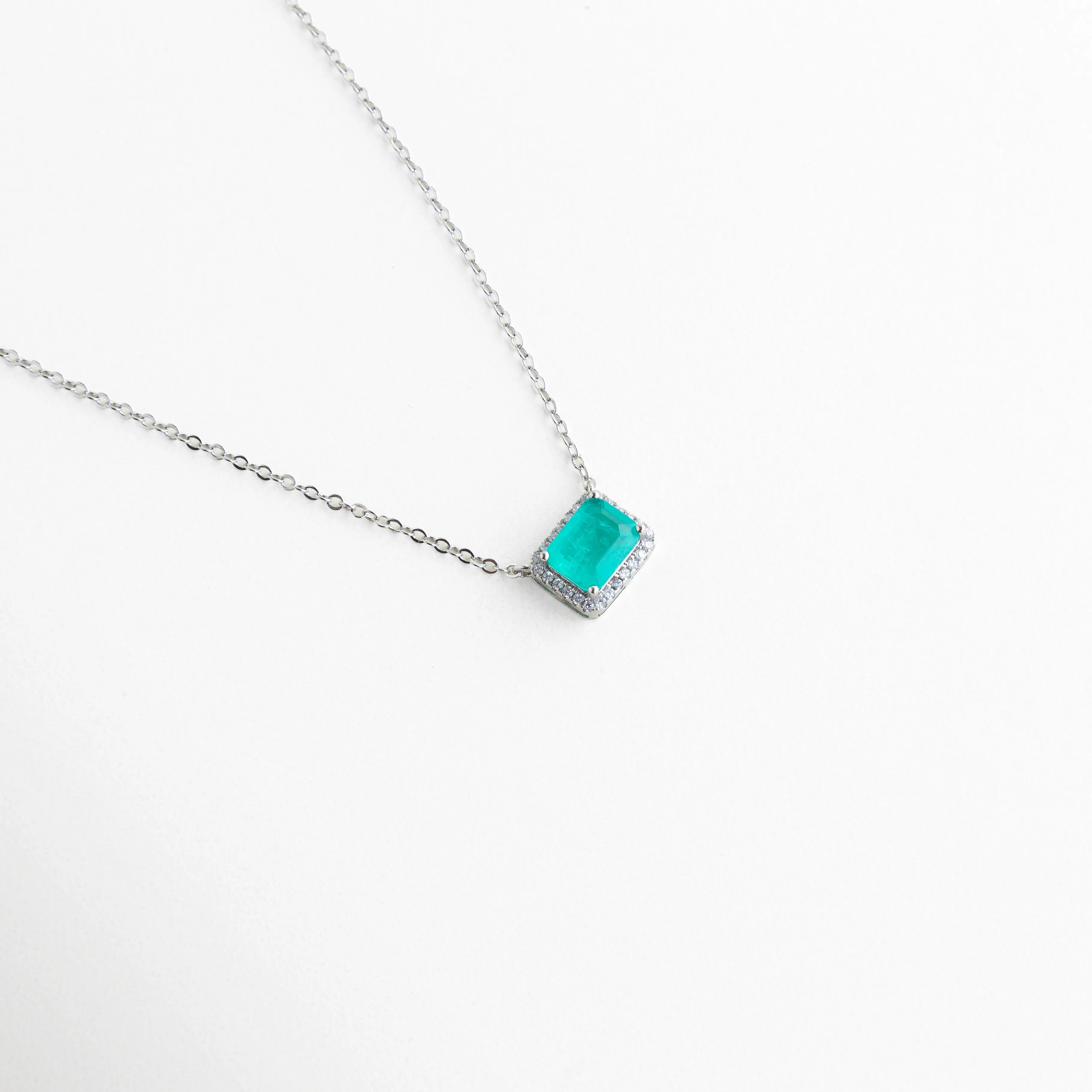 Dije de 1 cm color verde esmeralda montado en cadena de cobre enchapada, Collar delicado con piedra rectangular y halo de luz en acabado plateado, Vista en ángulo de joyería elegante con piedra verde para eventos especiales, Diseño moderno de collar con piedra esmeralda y marco de brillantes, Gargantilla con dije geométrico verde y recubrimiento de oro blanco 18K.
