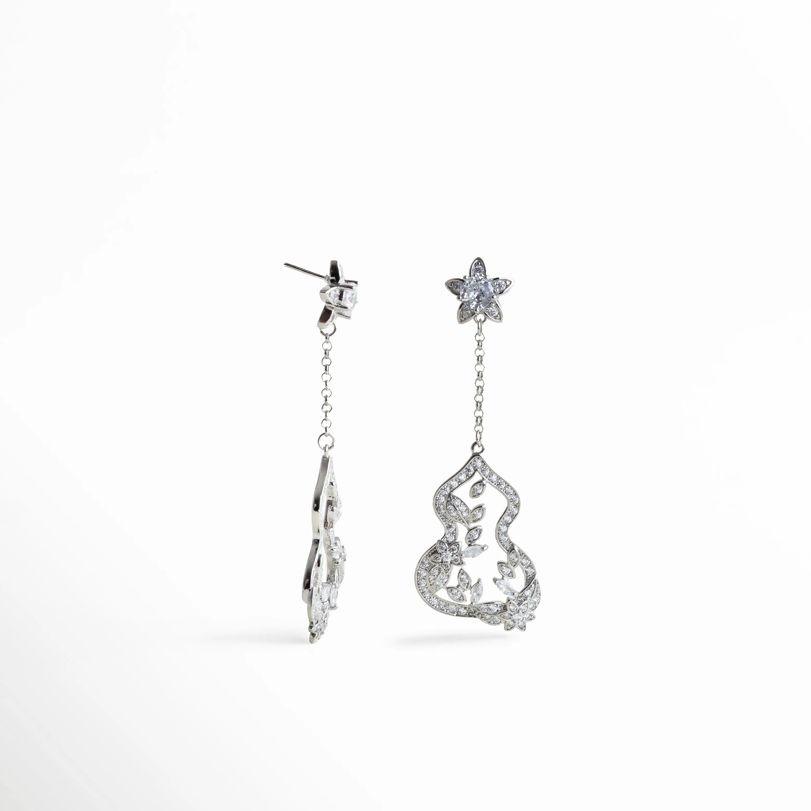 Aretes colgantes plateados con zirconias y detalle floral suspendido por cadena fina, mezcla de brillo y movimiento con acabado elegante.